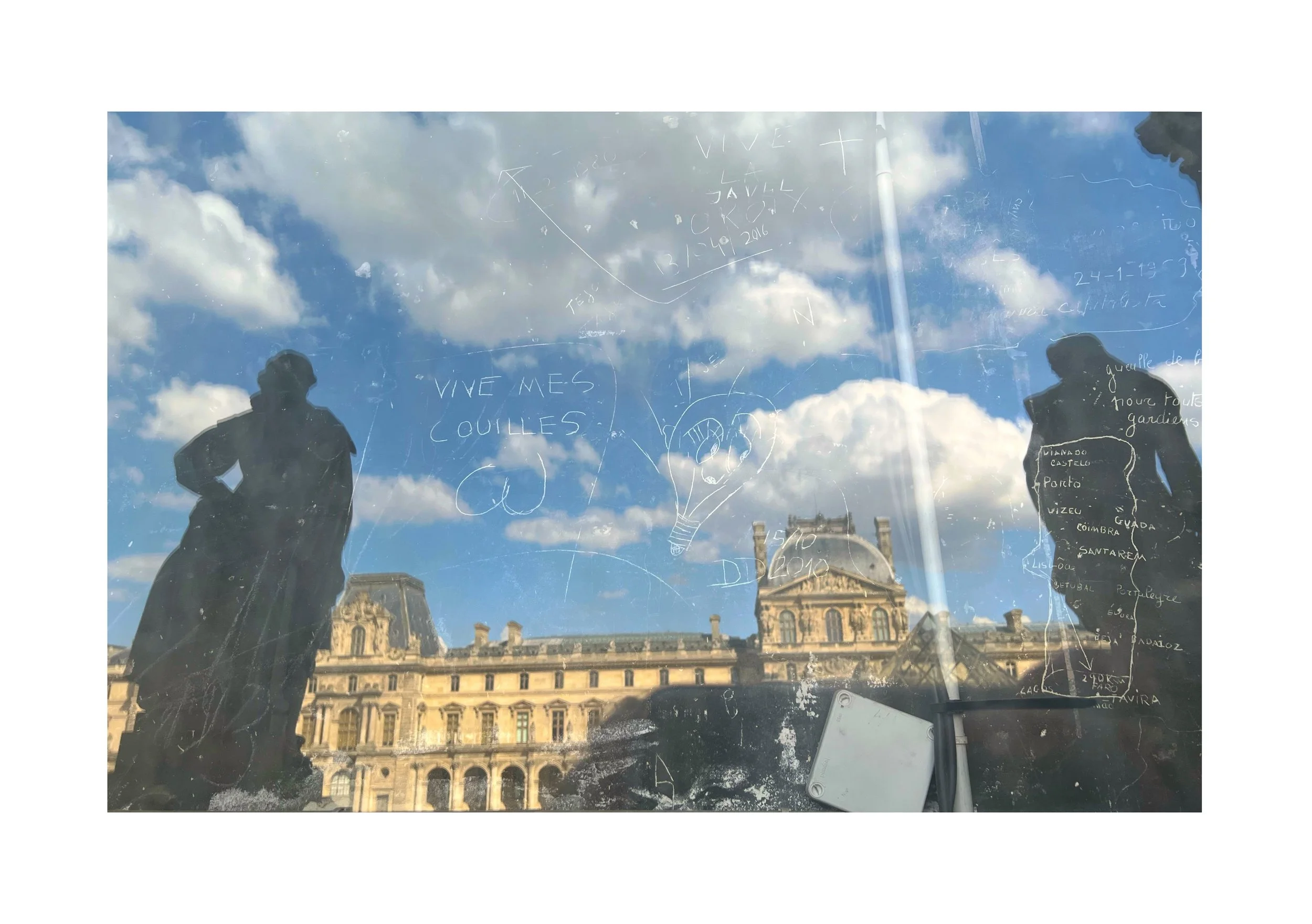 Reflet d'un bâtiment historique avec des silhouettes de deux personnes et des inscriptions écrites à la craie ou au marqueur sur une surface vitrée, avec un ciel bleu et des nuages en arrière-plan.