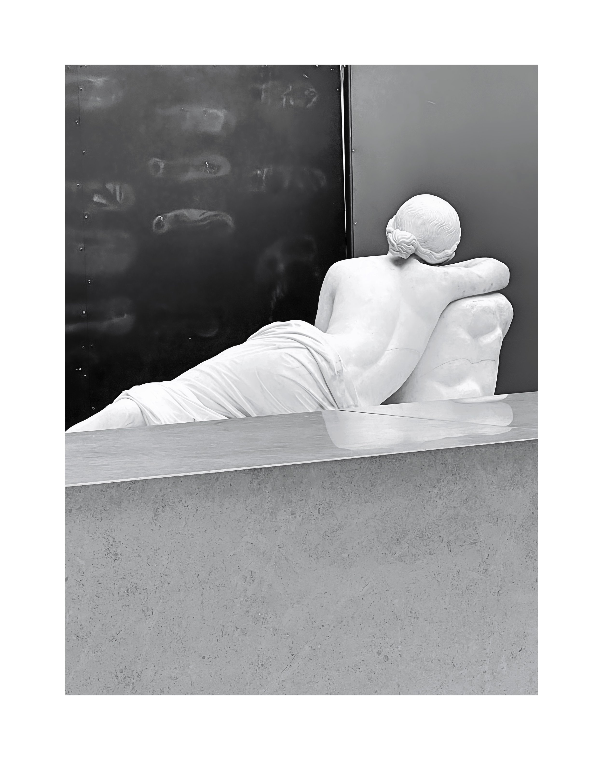 Statue de marbre d'une femme allongée, reposant contre une roche, vue de dos, dans un musée.