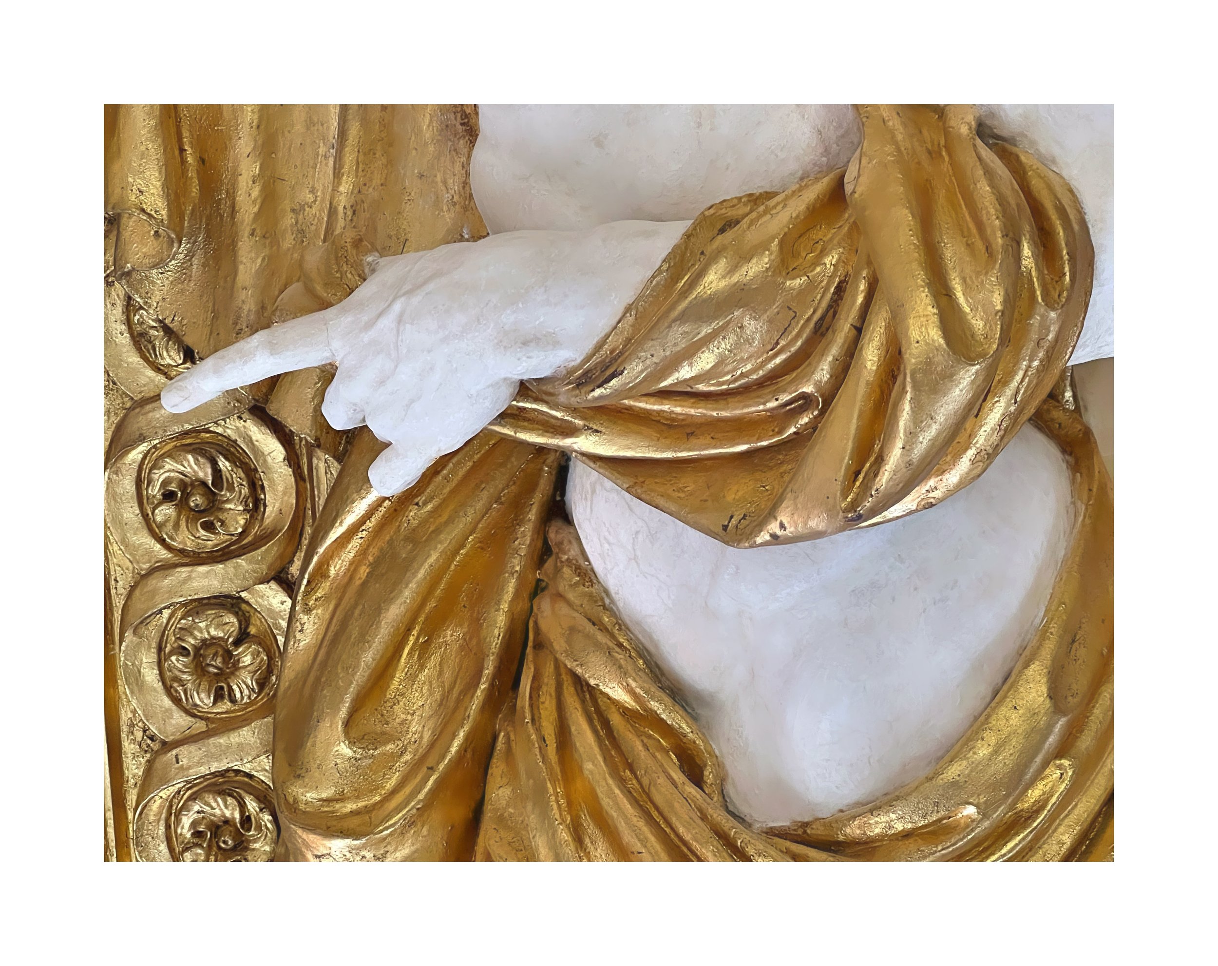 Détail d'une sculpture religieuse en or avec une main blanche touchant une robe dorée.