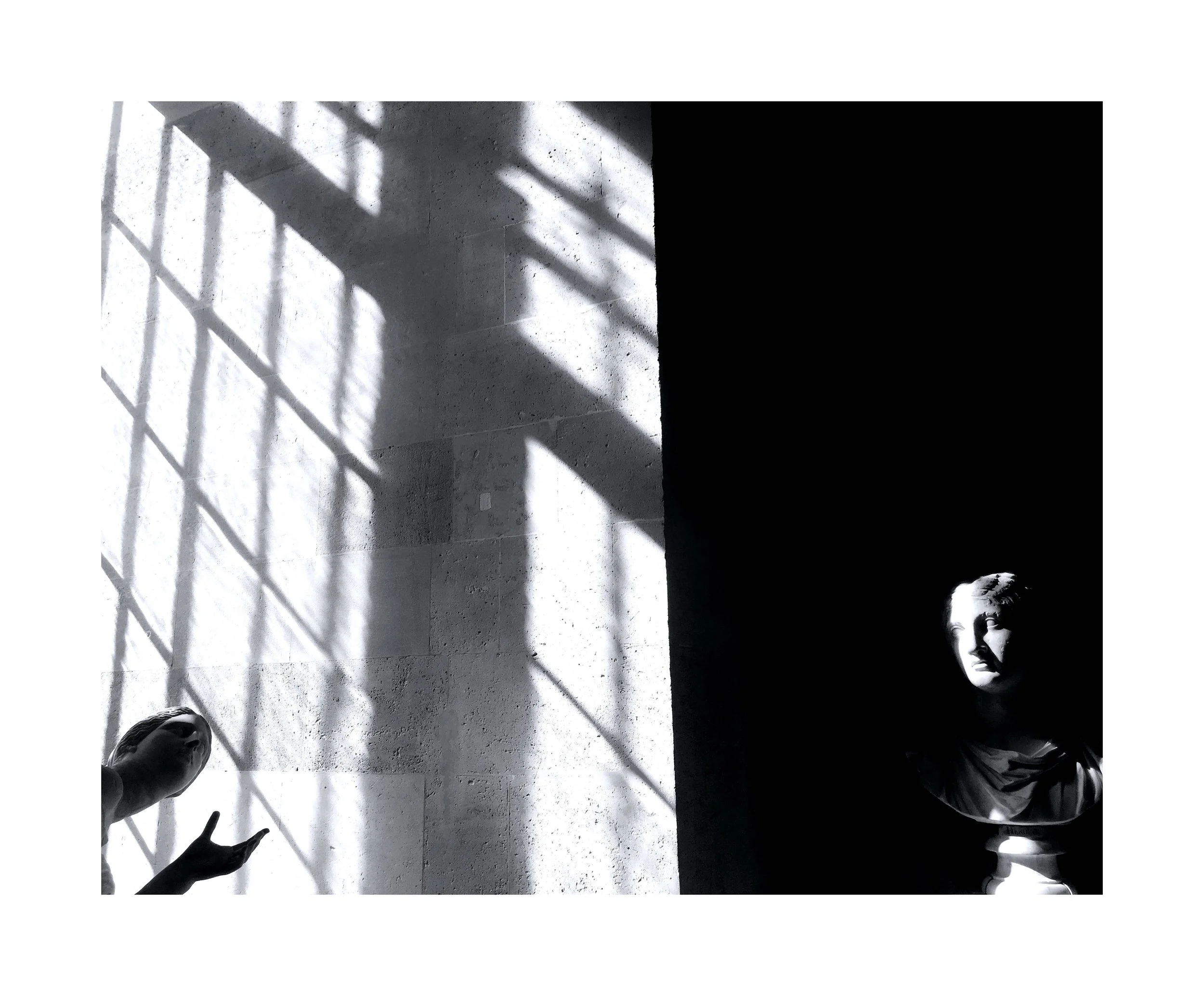 Une photographie en noir et blanc montrant deux bustes de statues. La statue à gauche a une main levée avec deux doigts pointés, tandis que la statue à droite est partiellement dans l'ombre.