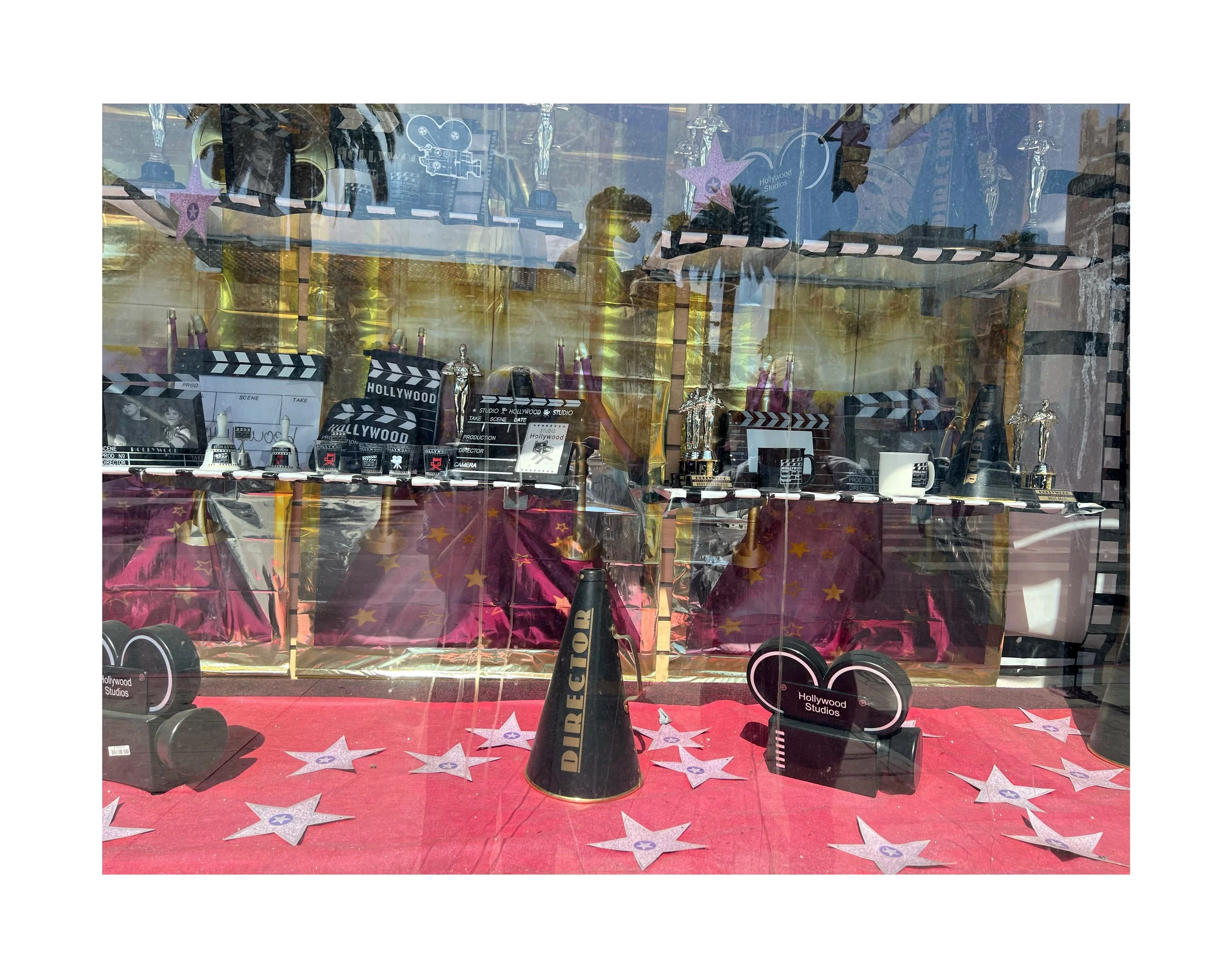 Vitrine décorée sur le thème hollywoodien avec trophées, chapitres de films, et accessoires liés au cinéma, sur un fond de papier à étoiles roses.