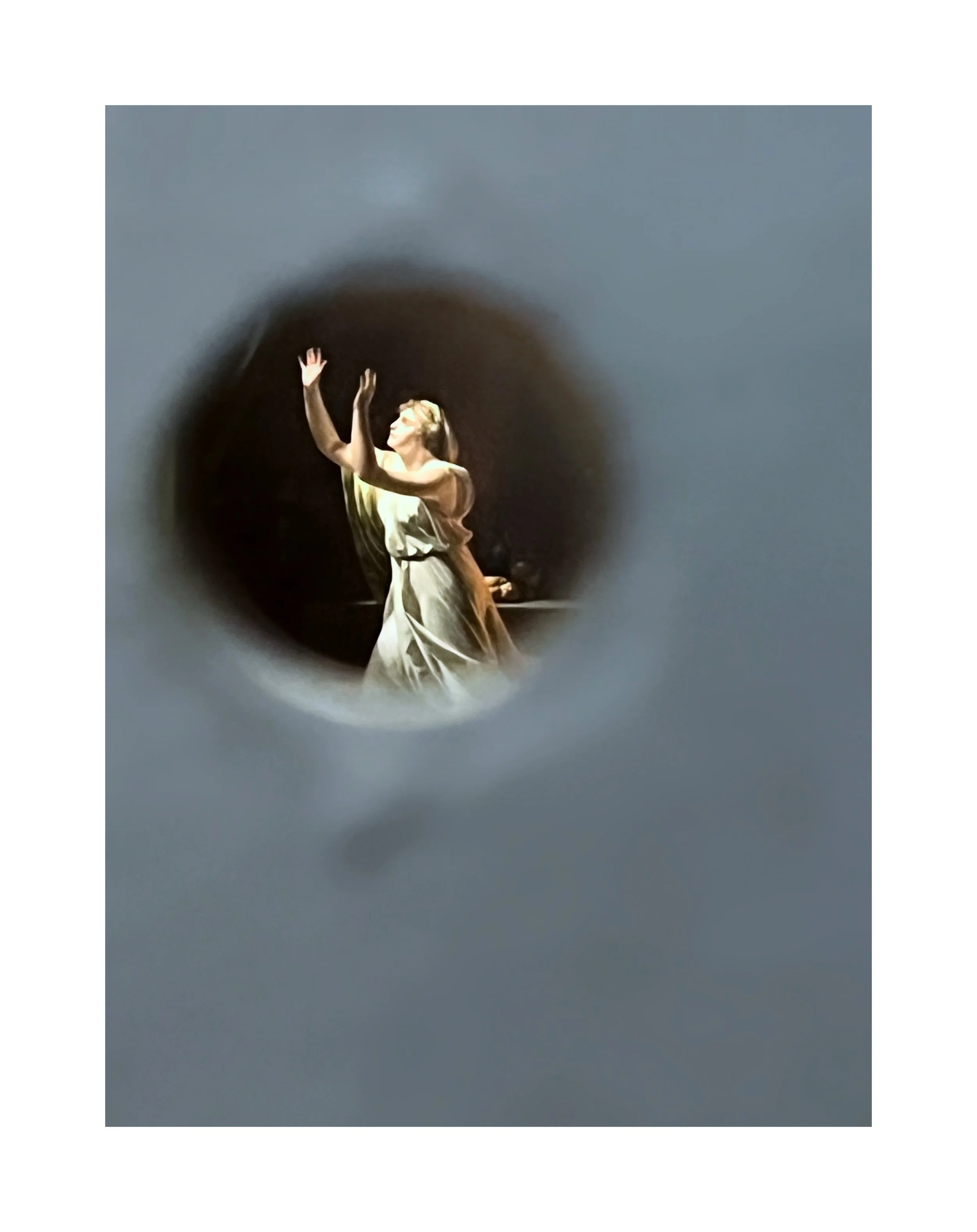 Une danseuse en robe de satin blanche, vue à travers un trou, effectue une pose expressive lors d'une performance sur scène.