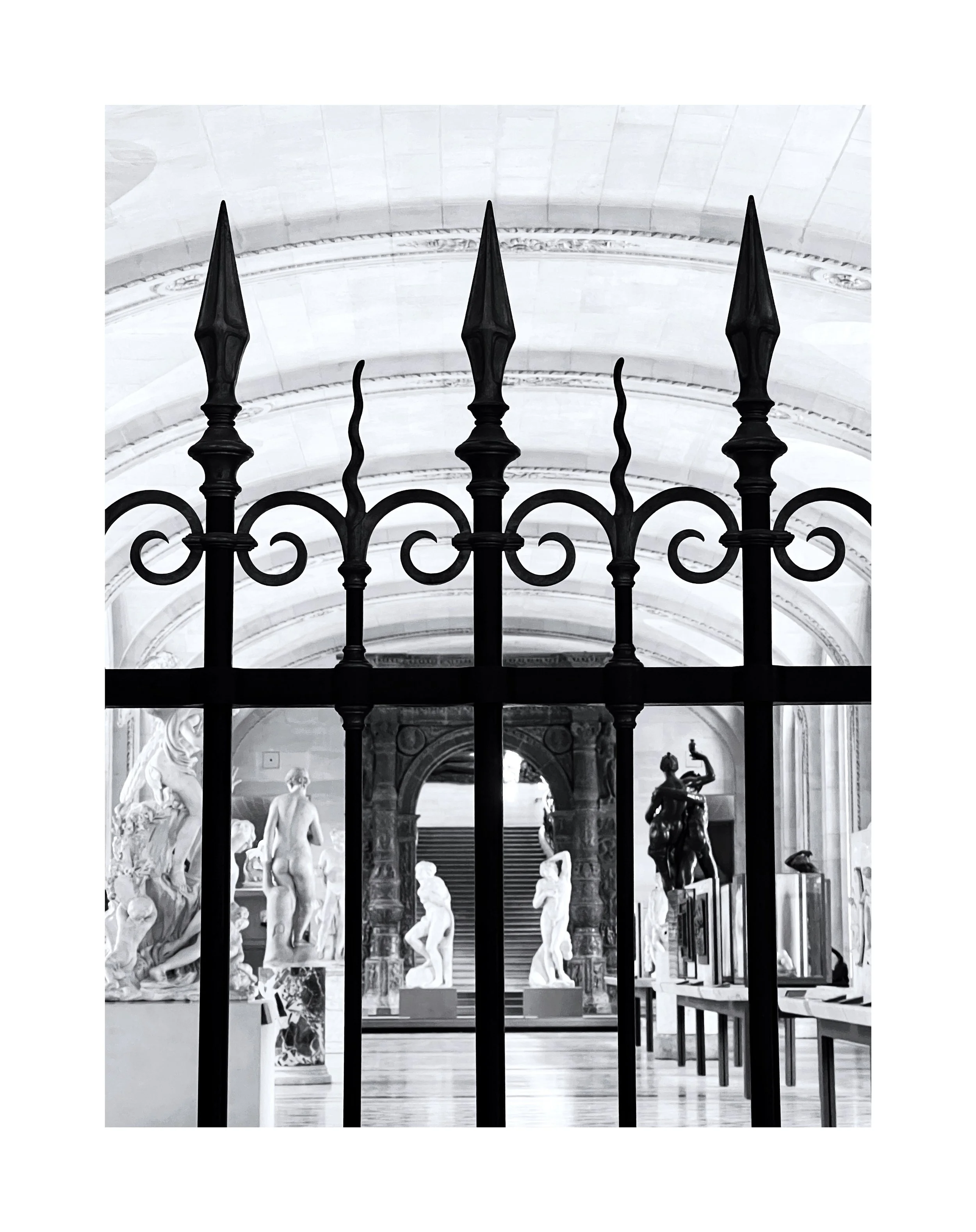 Une vue d'un musée d'art avec plusieurs sculptures classiques derrière une grille noire en fer forgé.