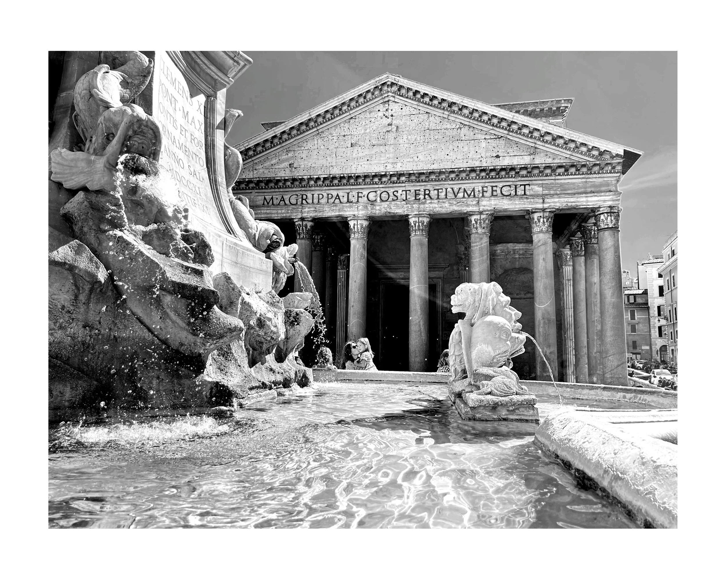 Une fontaine en pierre avec des sculptures de lions crachant de l'eau, devant un bâtiment ancien en style classique avec colonnes et une inscription en latin.