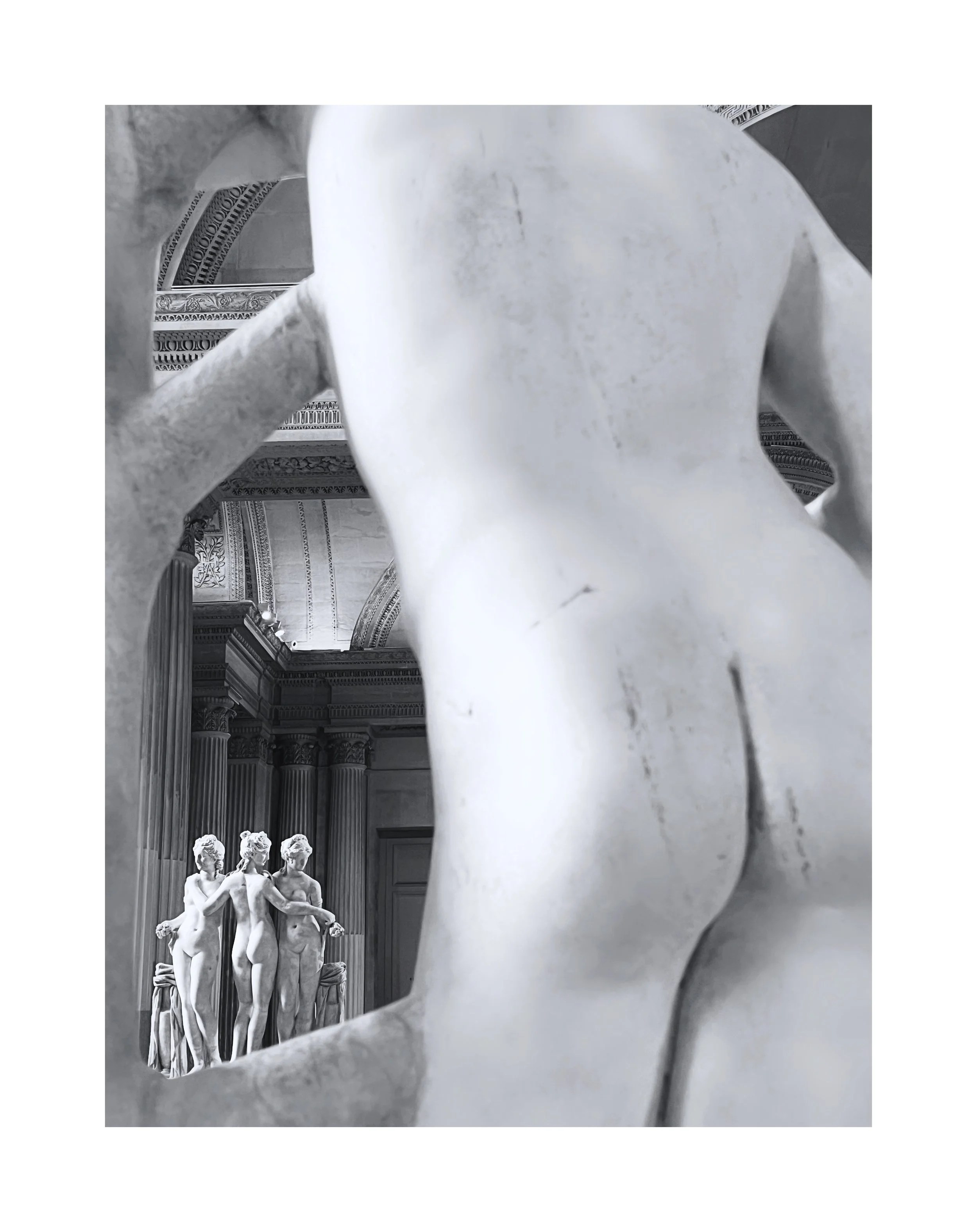 Vue artistique de statues en marbre, avec une sculpture en gros plan au premier plan et un groupe de trois statues en arrière-plan dans un intérieur architectural ornée.