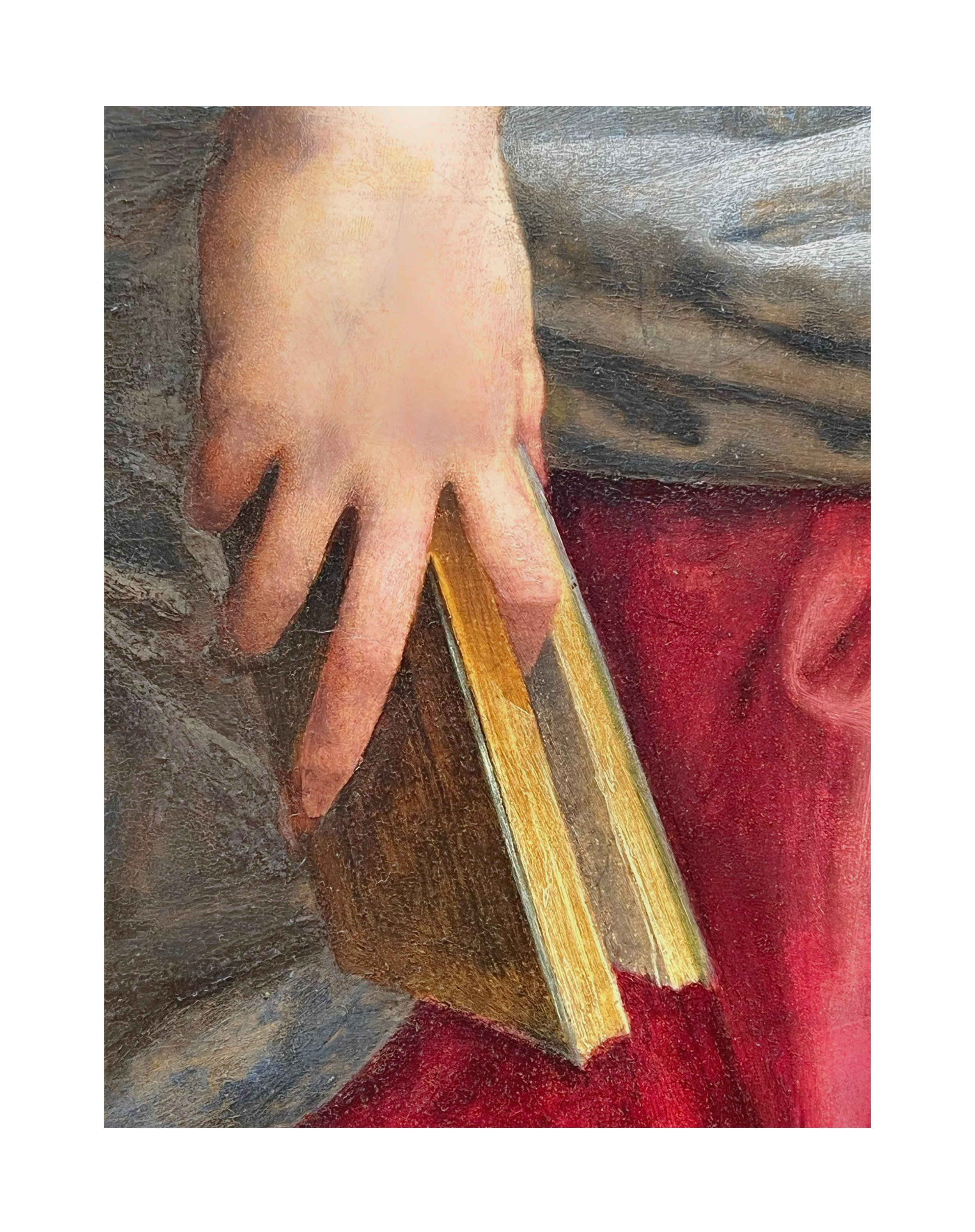 Une main posée sur un livre avec couverture en bois, vu de côté, avec une personne portant un vêtement gris et un pantalon rouge.