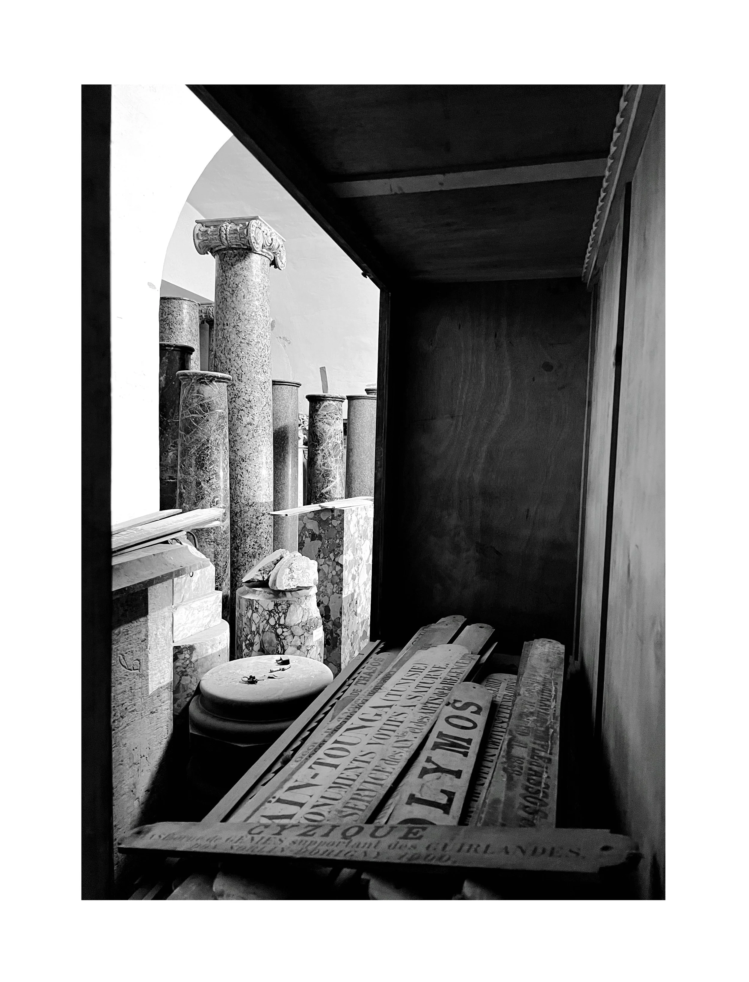 Vitrine contenant des objets anciens en marbre et en bois, dont des colonnes, des panneaux en bois et des inscriptions anciennes.