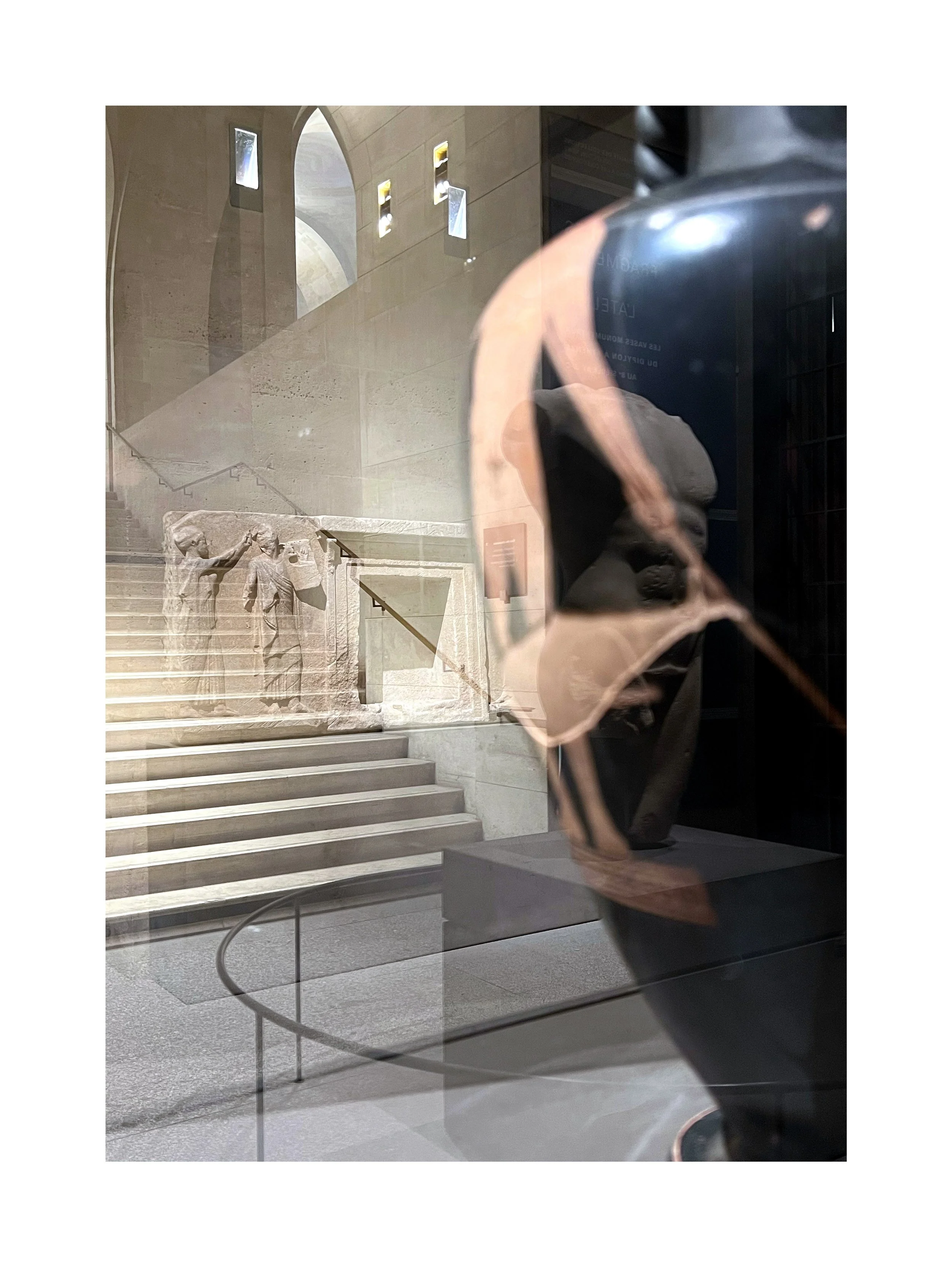 Reflet d'une sculpture dans une vitrine, avec un escalier en arrière-plan et un mur en pierre avec des fenêtres