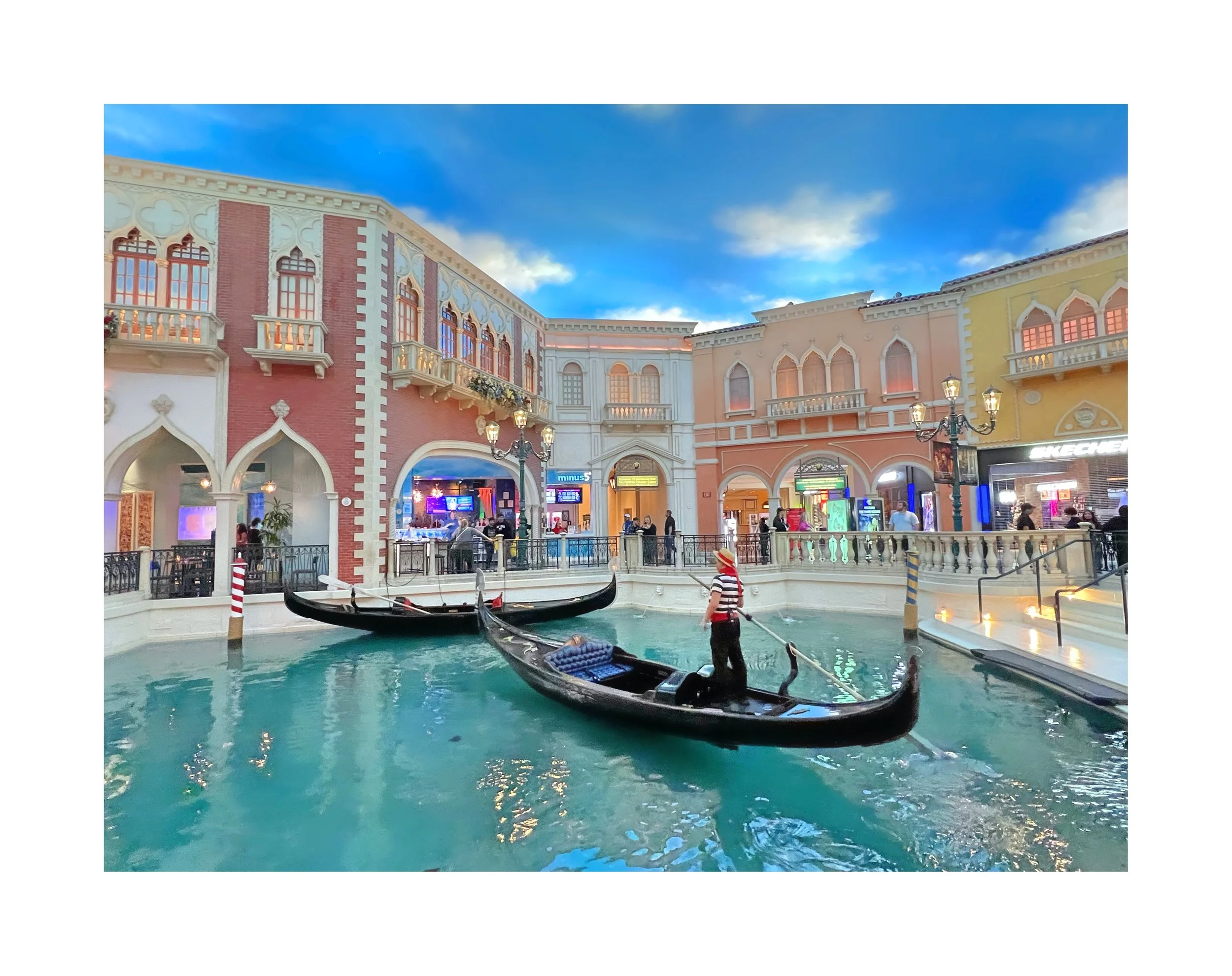 Voute de gondoles dans un canal intérieur, entouré de bâtiments de style européen, avec un ciel bleu et des nuages, dans un centre commercial ou une zone touristique.