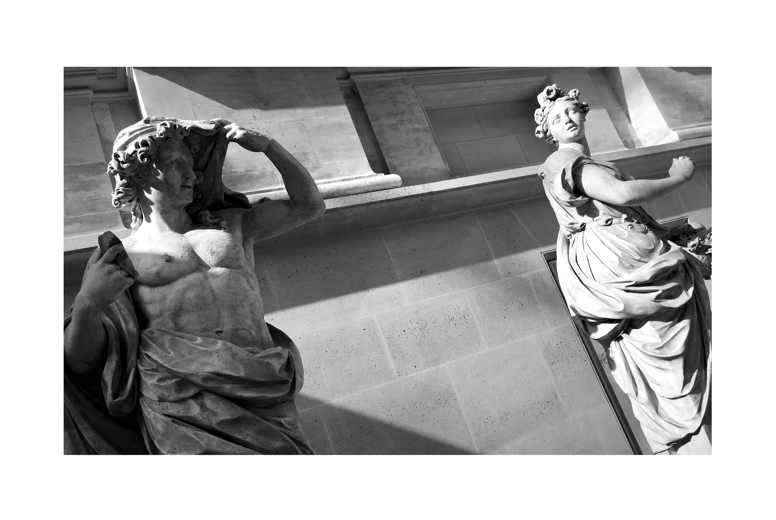 Sculptures en marbre d'un homme et d'une femme dans un musée, avec des jeux d'ombres et de lumières sur le mur en arrière-plan.