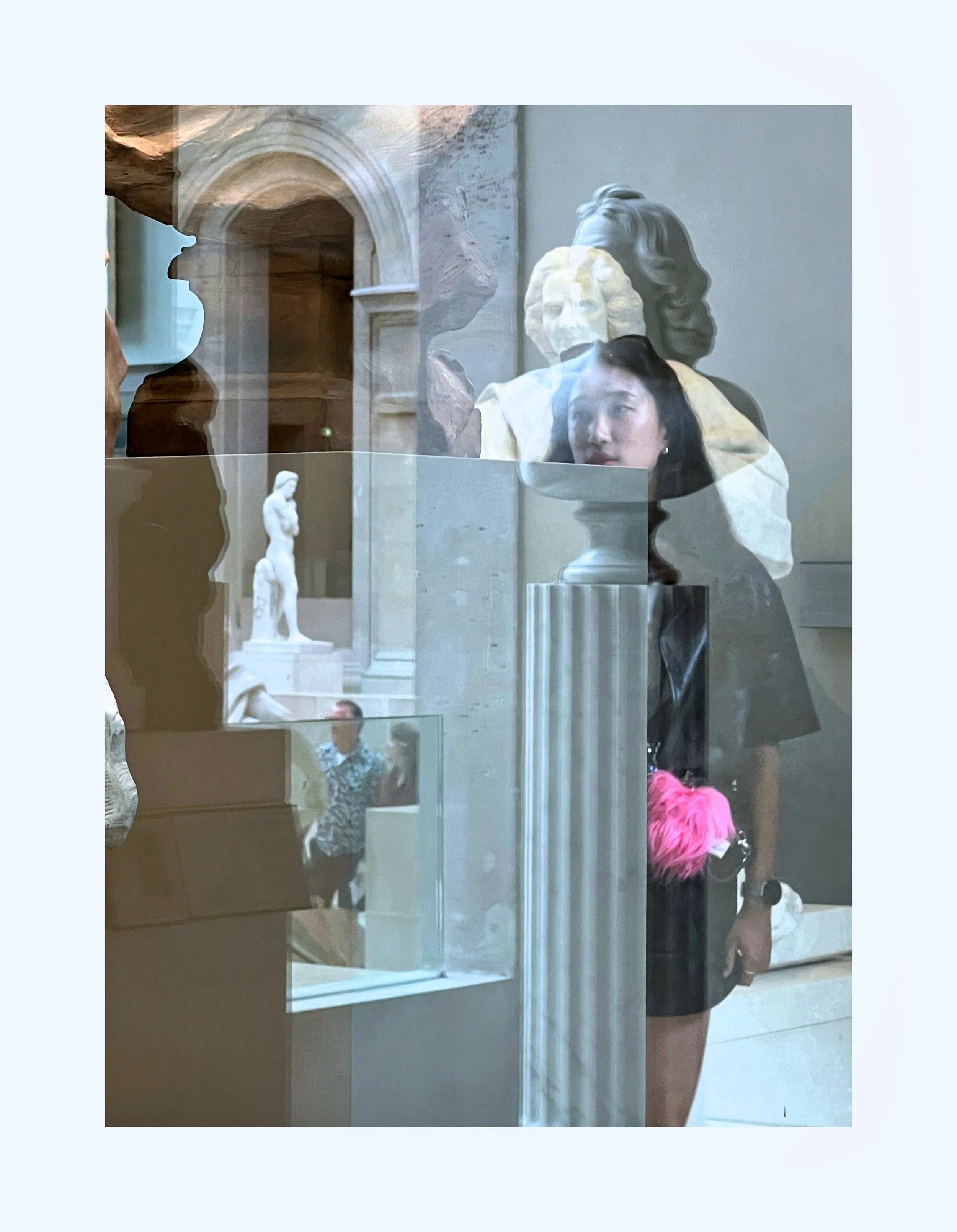 Reflet dans une vitrine d'un musée, montrant un mannequin avec une coiffure retro, une femmelette, un homme portant un t-shirt à motifs, et plusieurs statues antiques en arrière-plan.