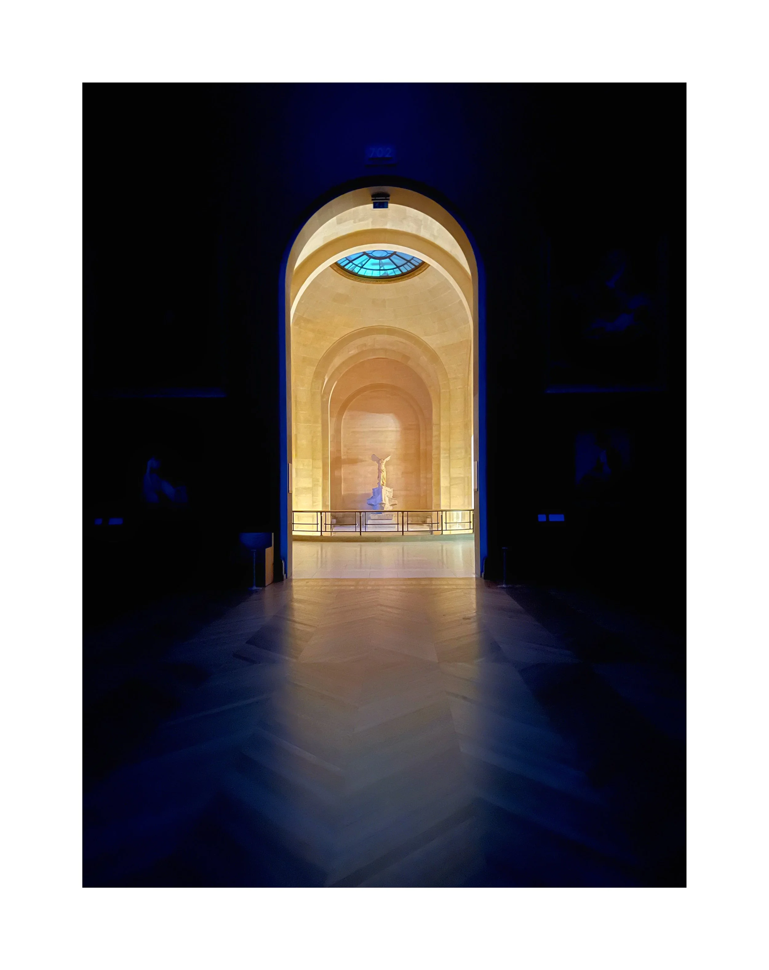 Vue intérieure d'une église ou musée avec un cercueil ou une sculpture dorée au centre de l'alcôve, encadrée par un arc et éclairée par un puits de lumière bleue depuis le plafond.