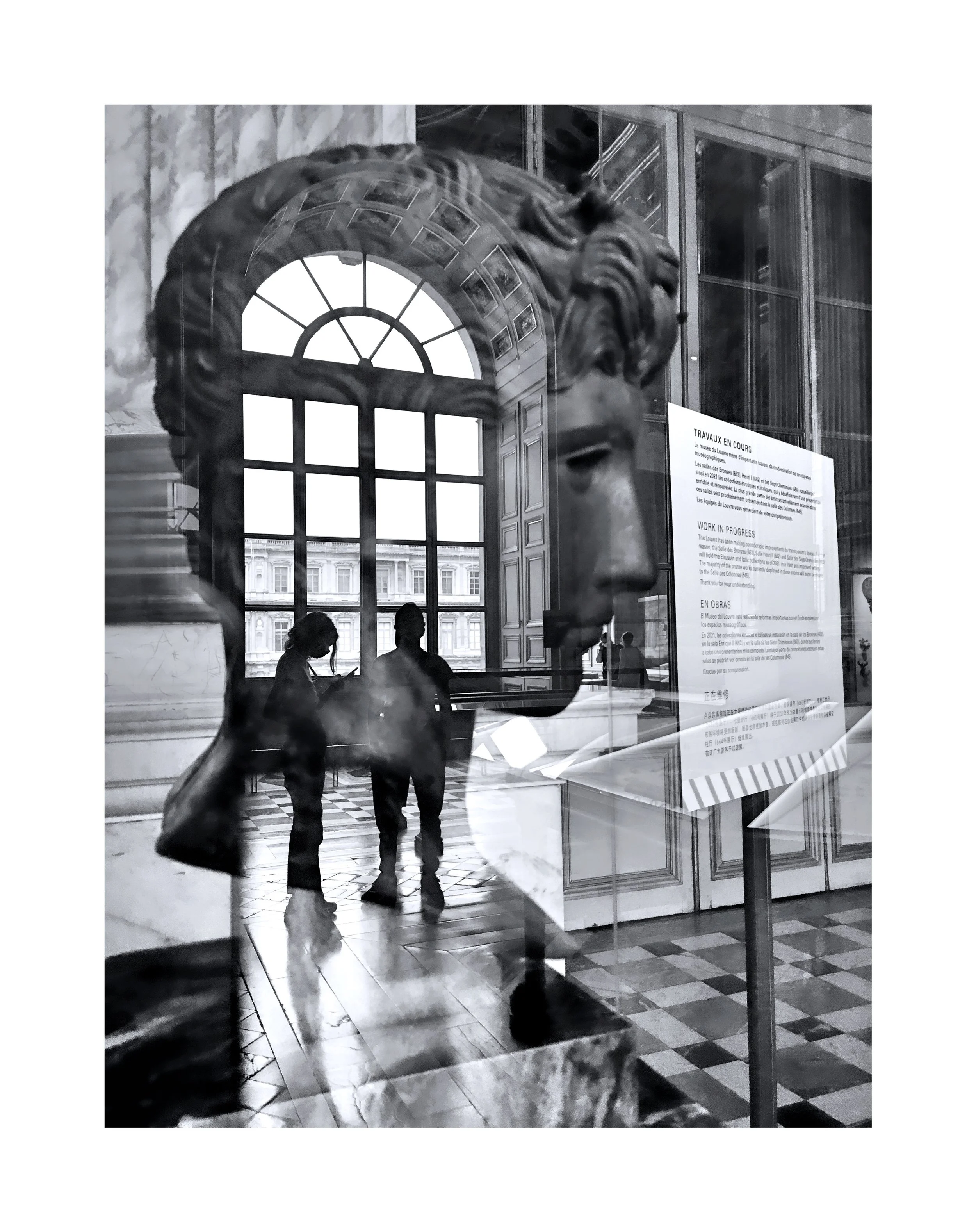 Une sculpture de lion en bronze, vue à travers une vitre, dans un musée, avec des personnes en train de regarder une affiche d'information.