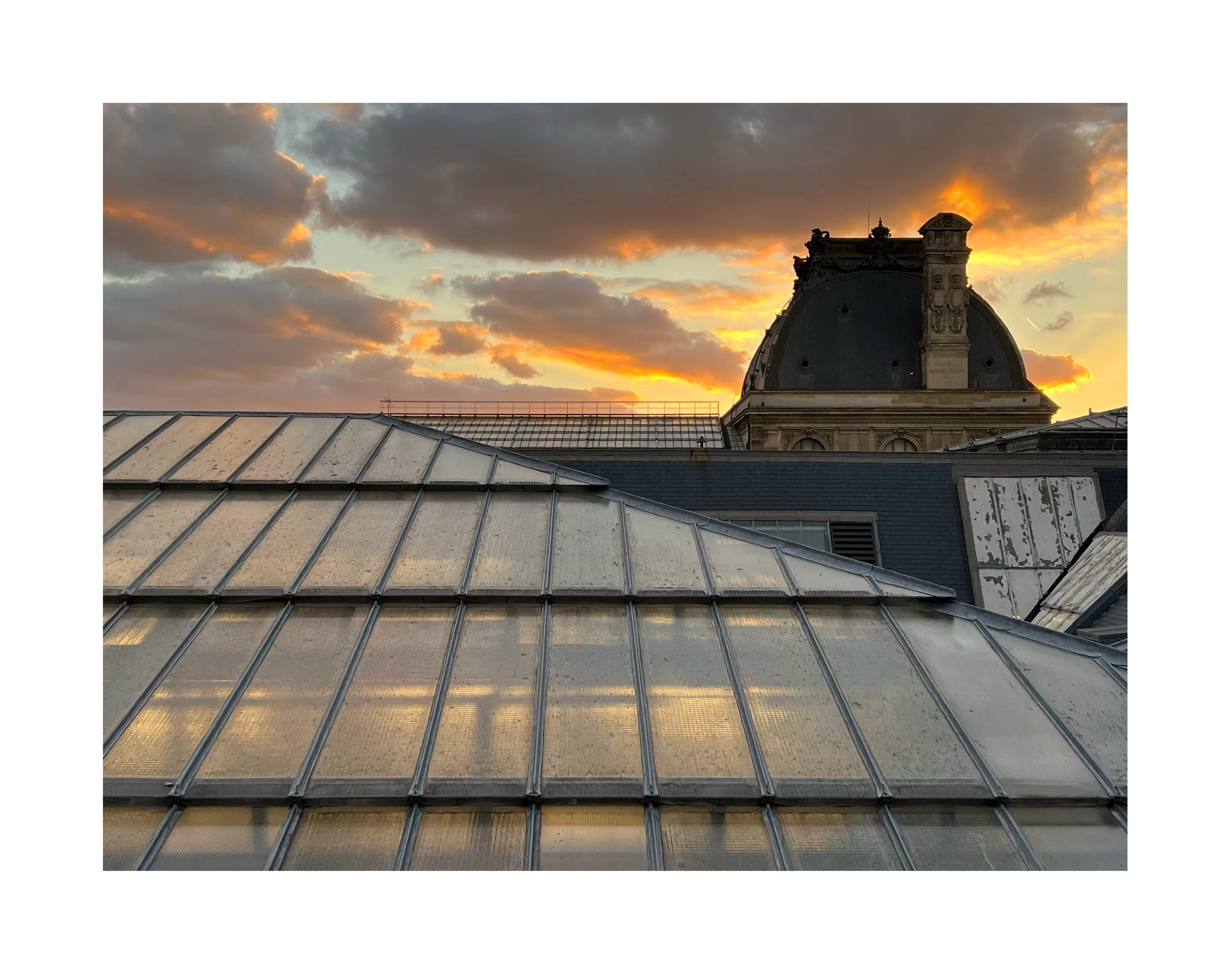 Cadrage sur un toit en verre avec un ciel orageux au coucher du soleil et un dôme historique en arrière-plan.