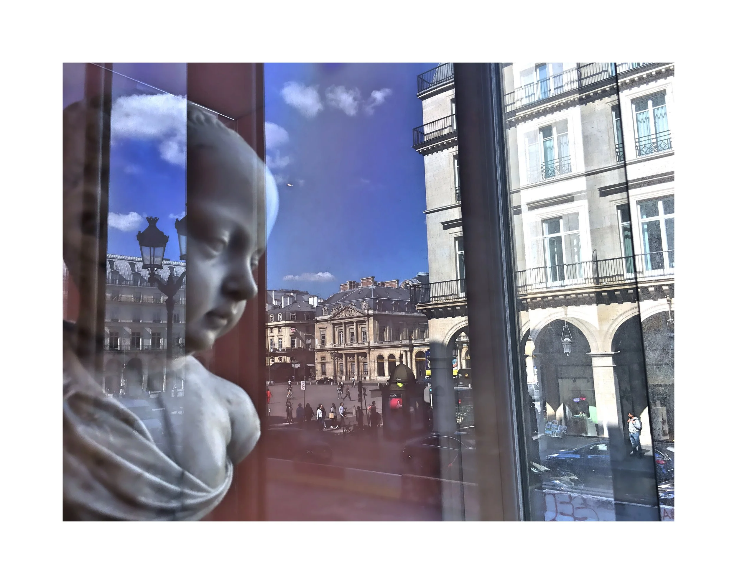 Vue à travers une fenêtre d'un bâtiment montrant un enfant en plâtre, une rue animée avec des passants et des bâtiments de style haussmannien en arrière-plan, sous un ciel bleu avec quelques nuages.