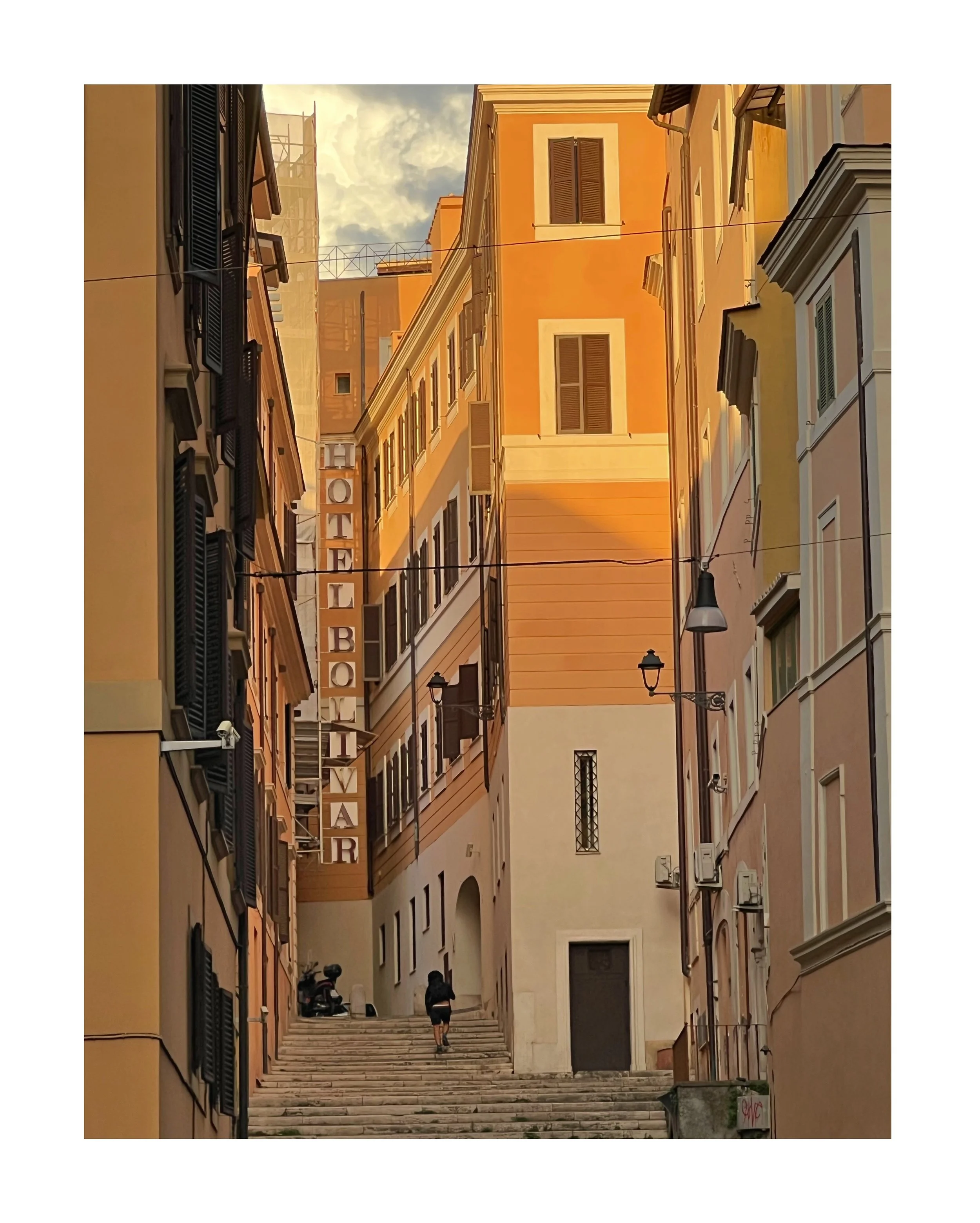 Vue d'une ruelle étroite avec des bâtiments de couleur jaune et beige, un escalier en pierre menant à une rue en hauteur, et un panneau indiquant 'HOTEL BOLIVAR'.