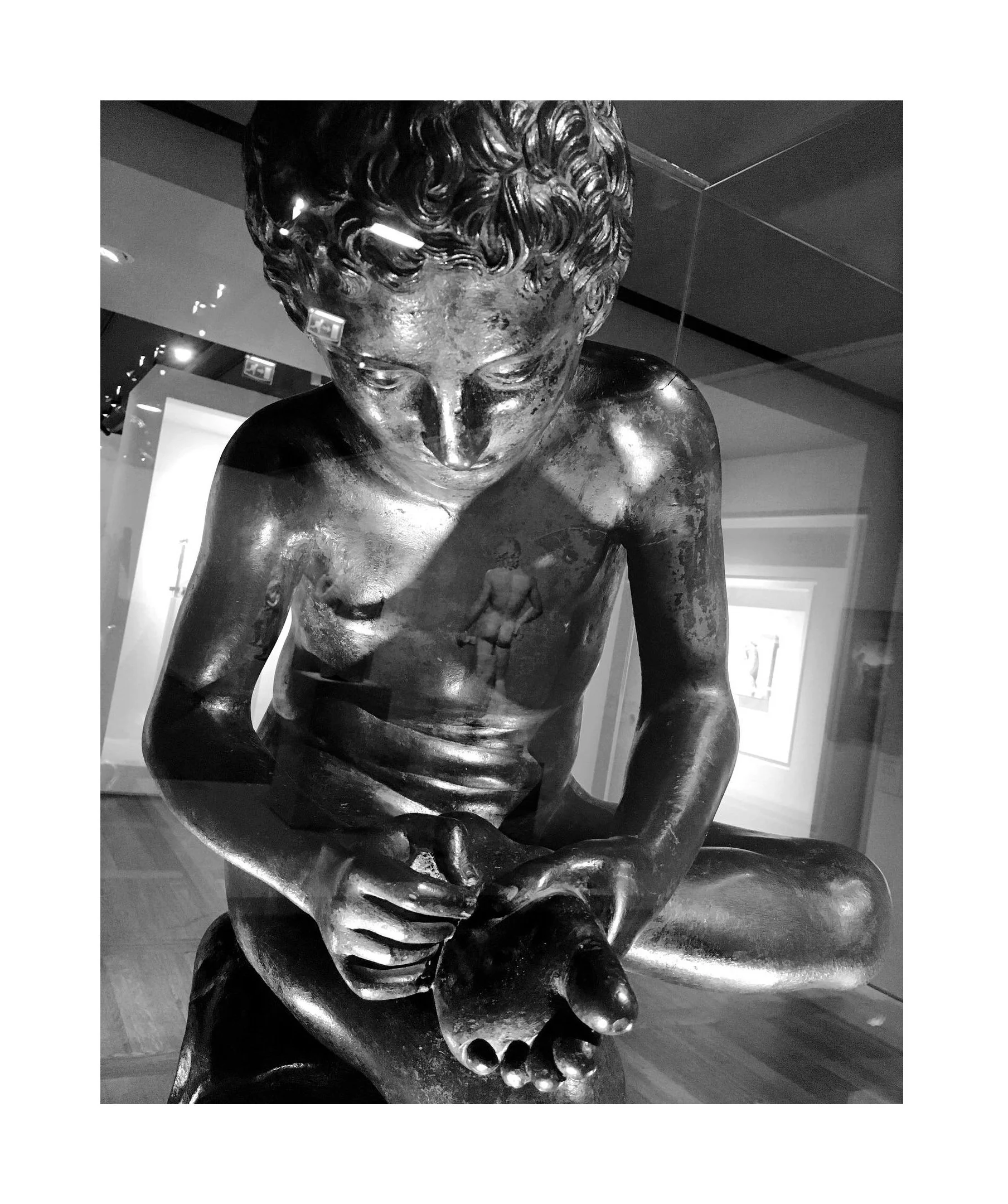 Sculpture en bronze d'un enfant assis, avec un trou dans la main, exposée dans un musée, vue en gros plan.