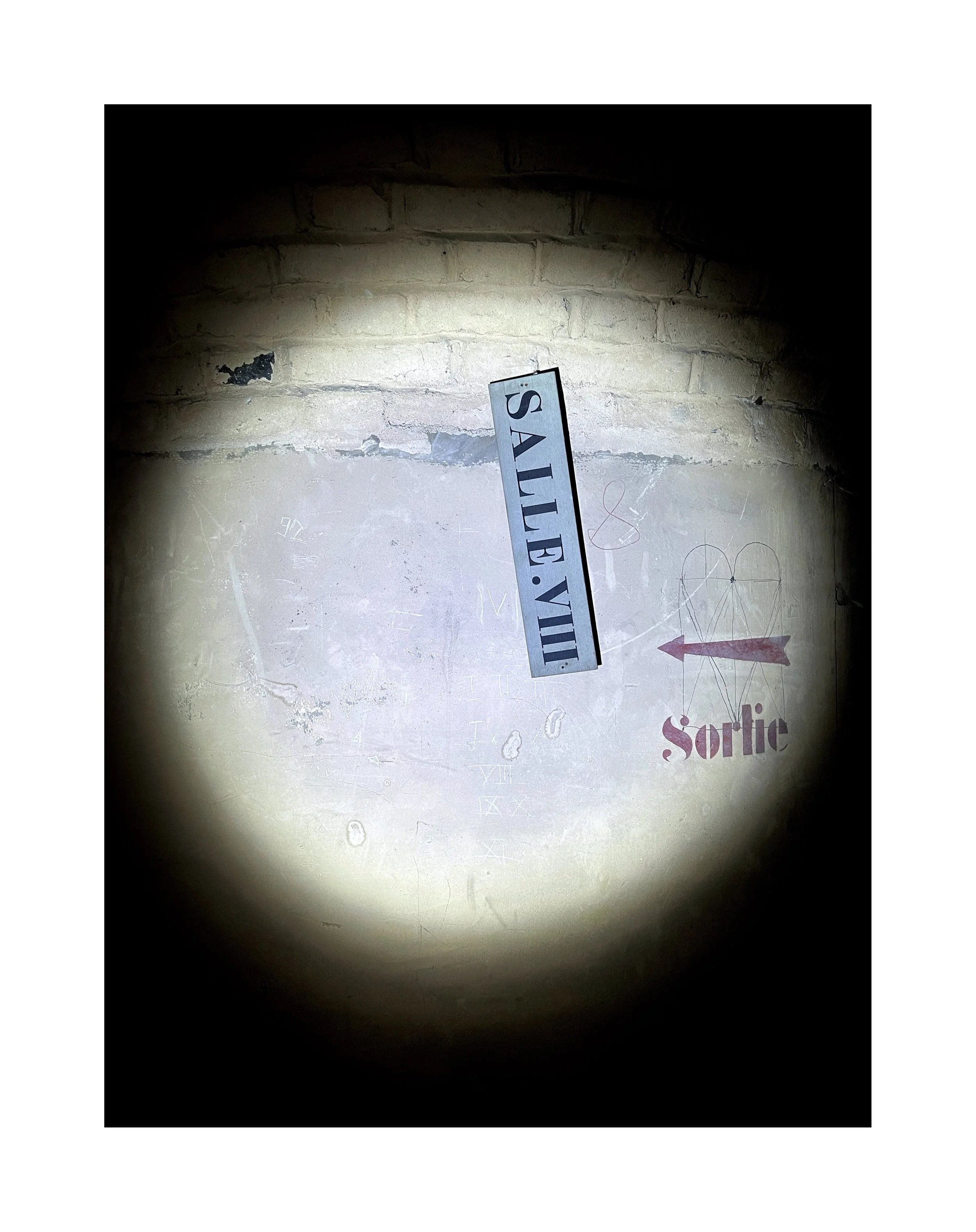 Une affiche lumineuse indique « SALE: VIII », une peinture murale en arrière-plan montre une flèche rouge pointant vers la droite avec le mot « Sortie » en dessous, et une surface de mur en pierre est partiellement visible.