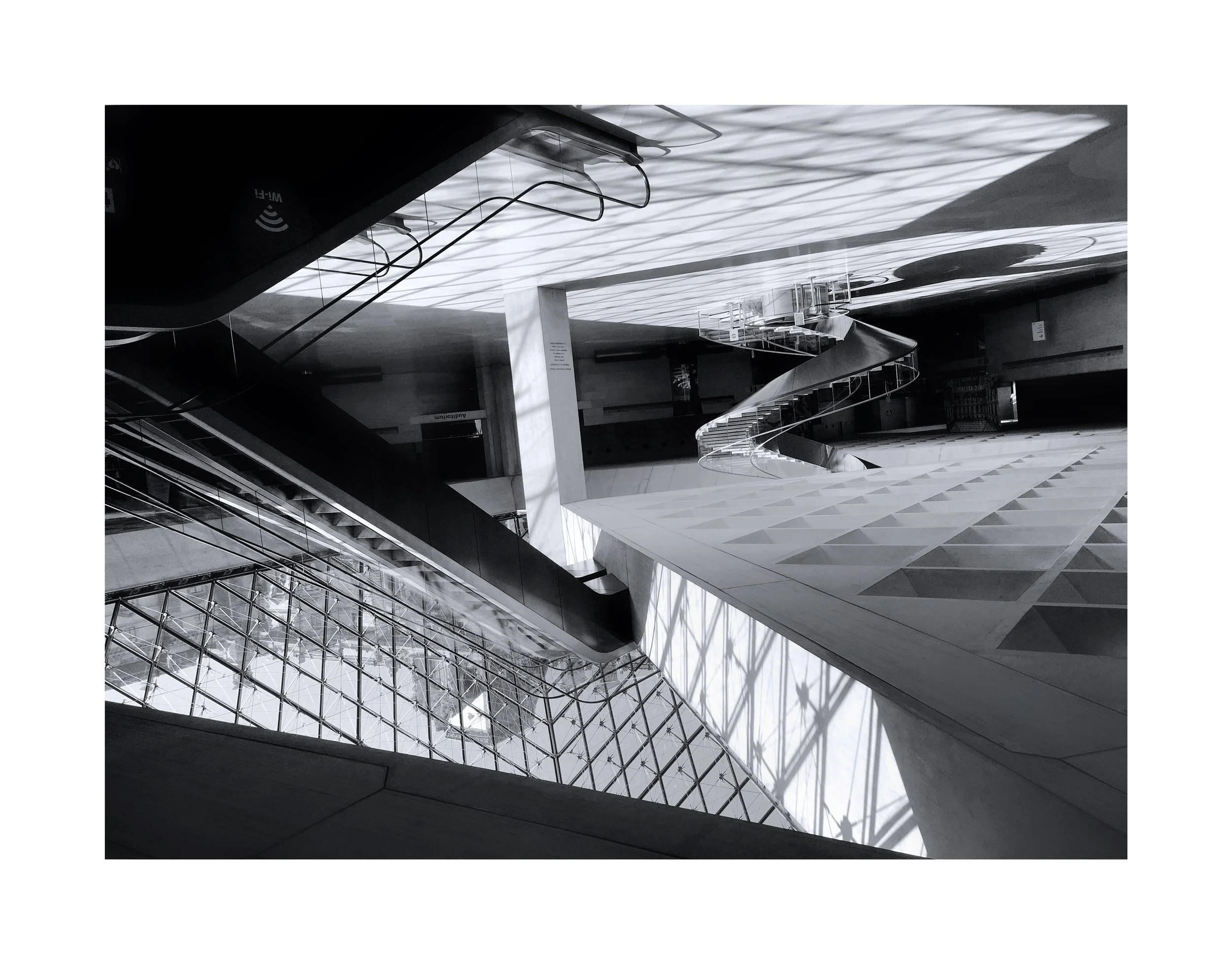 Intérieur d'un bâtiment moderne avec une escalier en colimaçon, une structure en verre et des ombres de lumière sur le plafond.