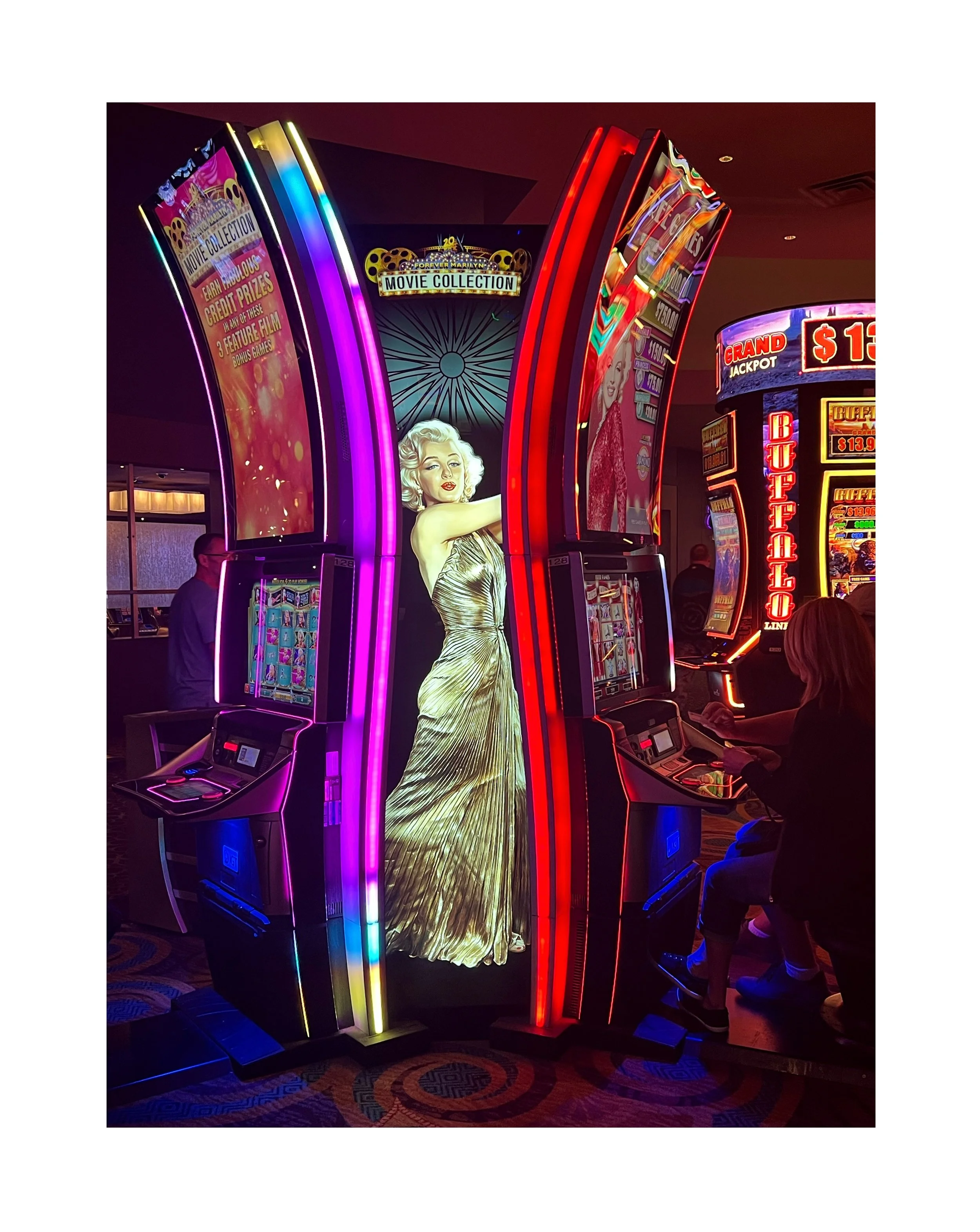  Machines à sous dans un casino avec une image géante de Marilyn Monroe en fond, décor lumineux et plusieurs personnes jouant.