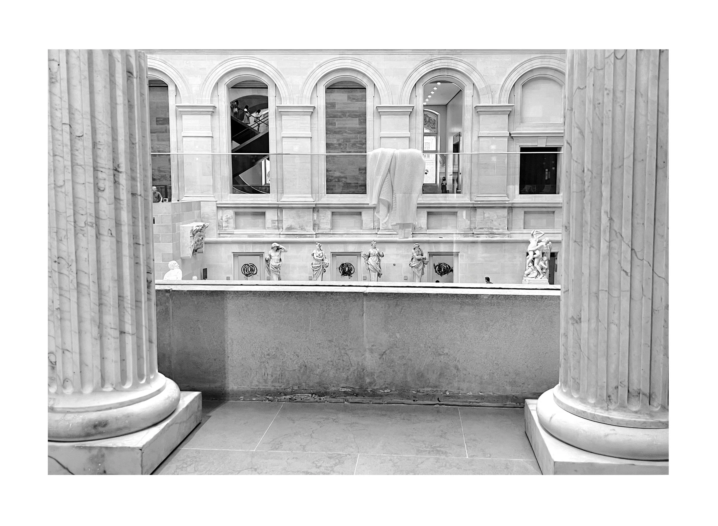 Vue intérieure d'un musée avec colonnes en marbre, sculptures classiques, fenêtres en arc et tissu suspendu.