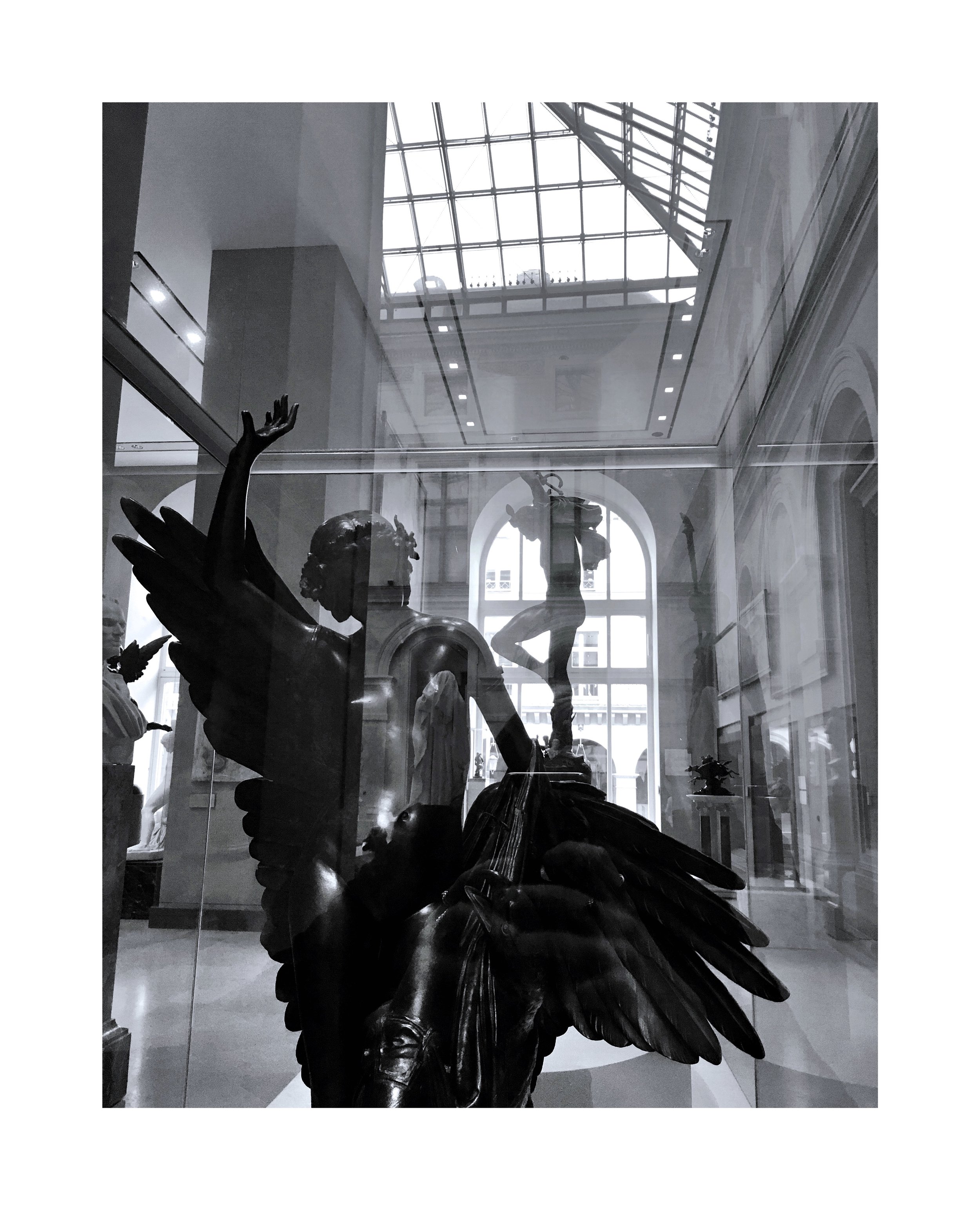 Statues en bronze dans le musée, avec un reflet dans la vitre et un plafond en verre au-dessus.