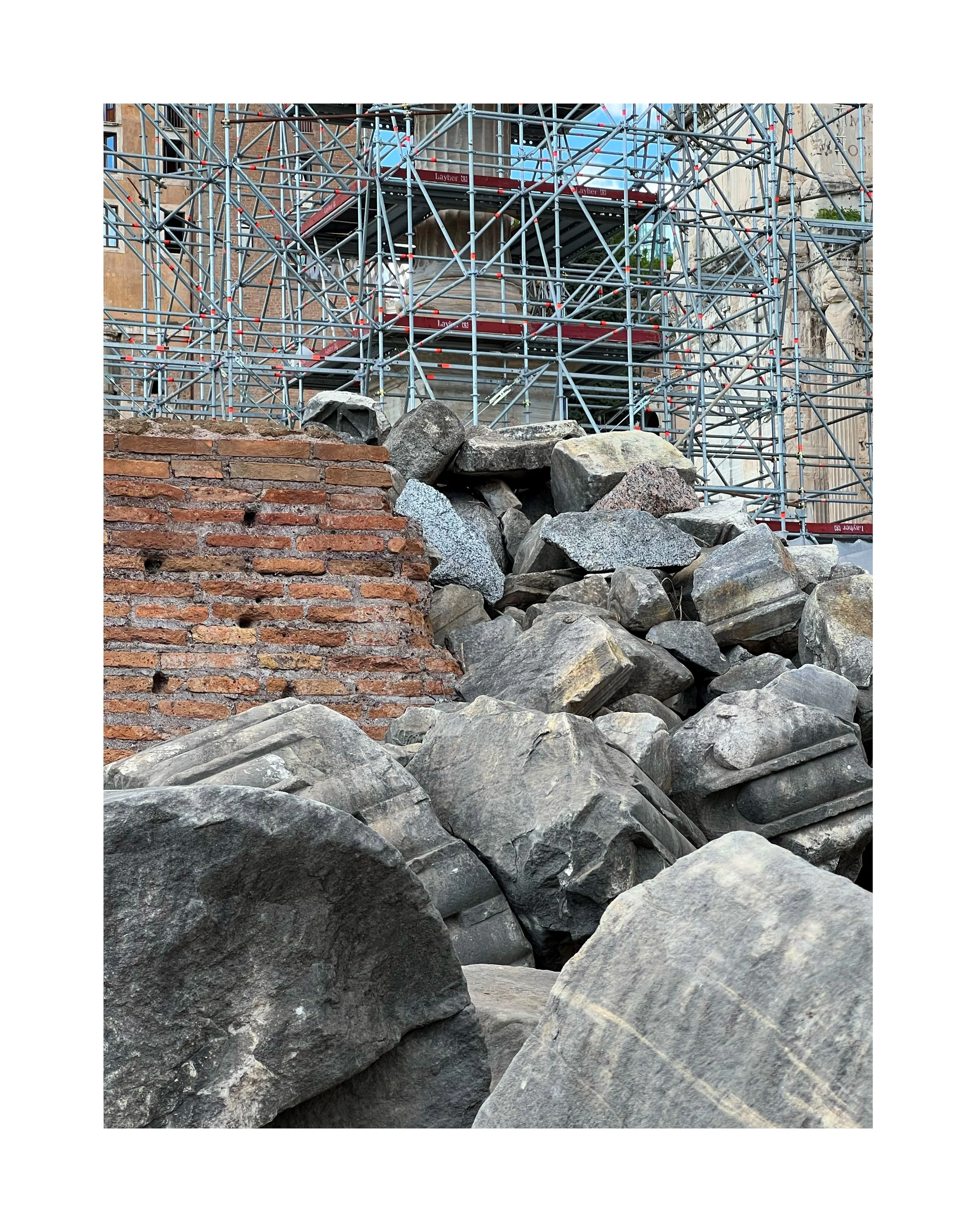 Monticule de grosses pierres et morceaux de brique devant une structure de scaffolding en métal rouge, en zone urbaine.