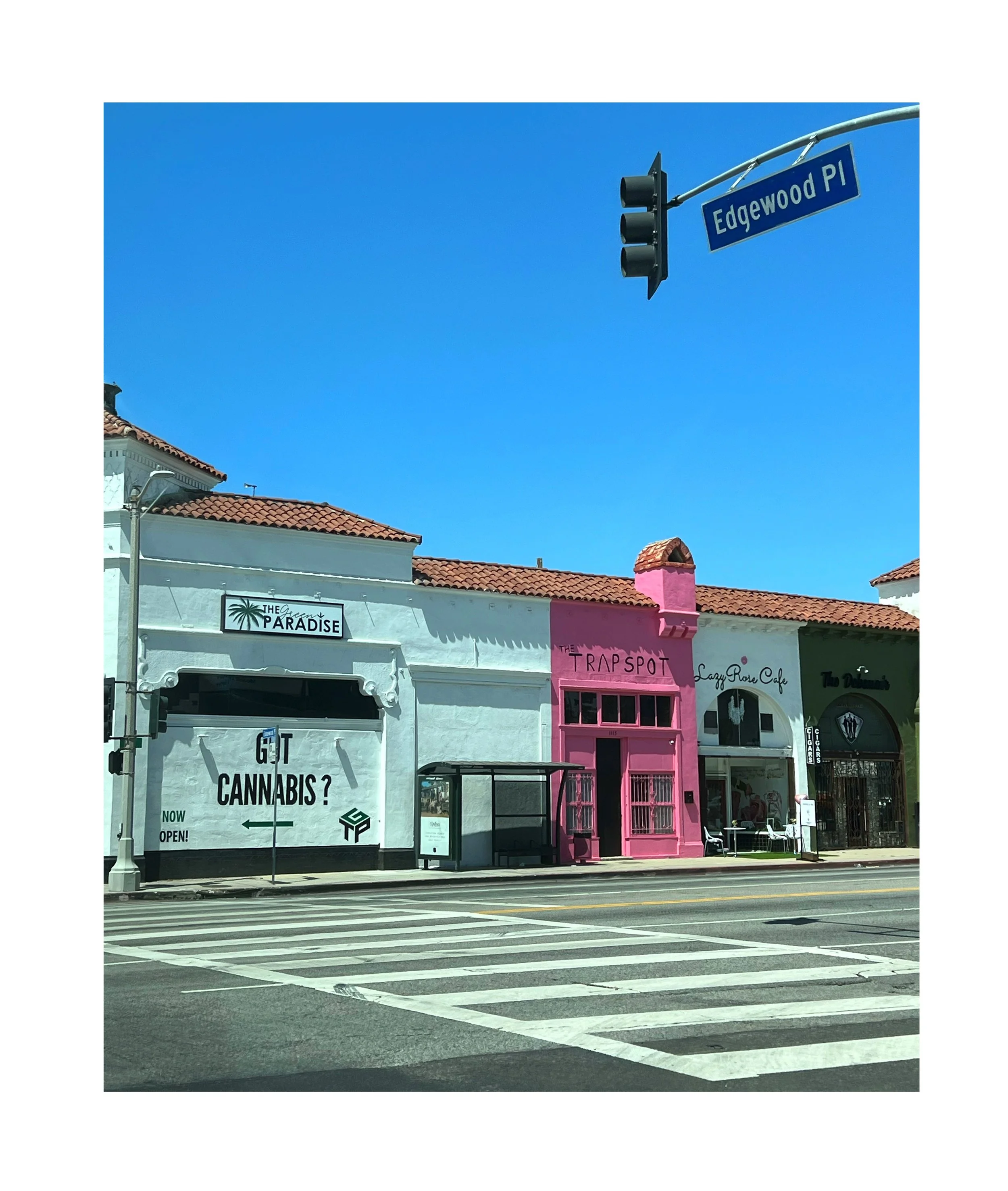 Rue Edgewood avec des boutiques colorées, y compris un magasin de cannabis, un café au nom de The Trapspot, un autre café Laguna Rose, et un point d'arrêt de bus à l'arrêt.