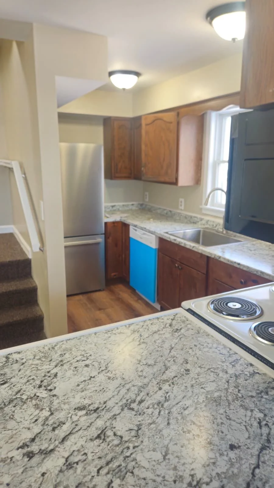 Kitchen with wooden cabinets, granite countertops, stainless steel refrigerator, stove, and a window above the sink.