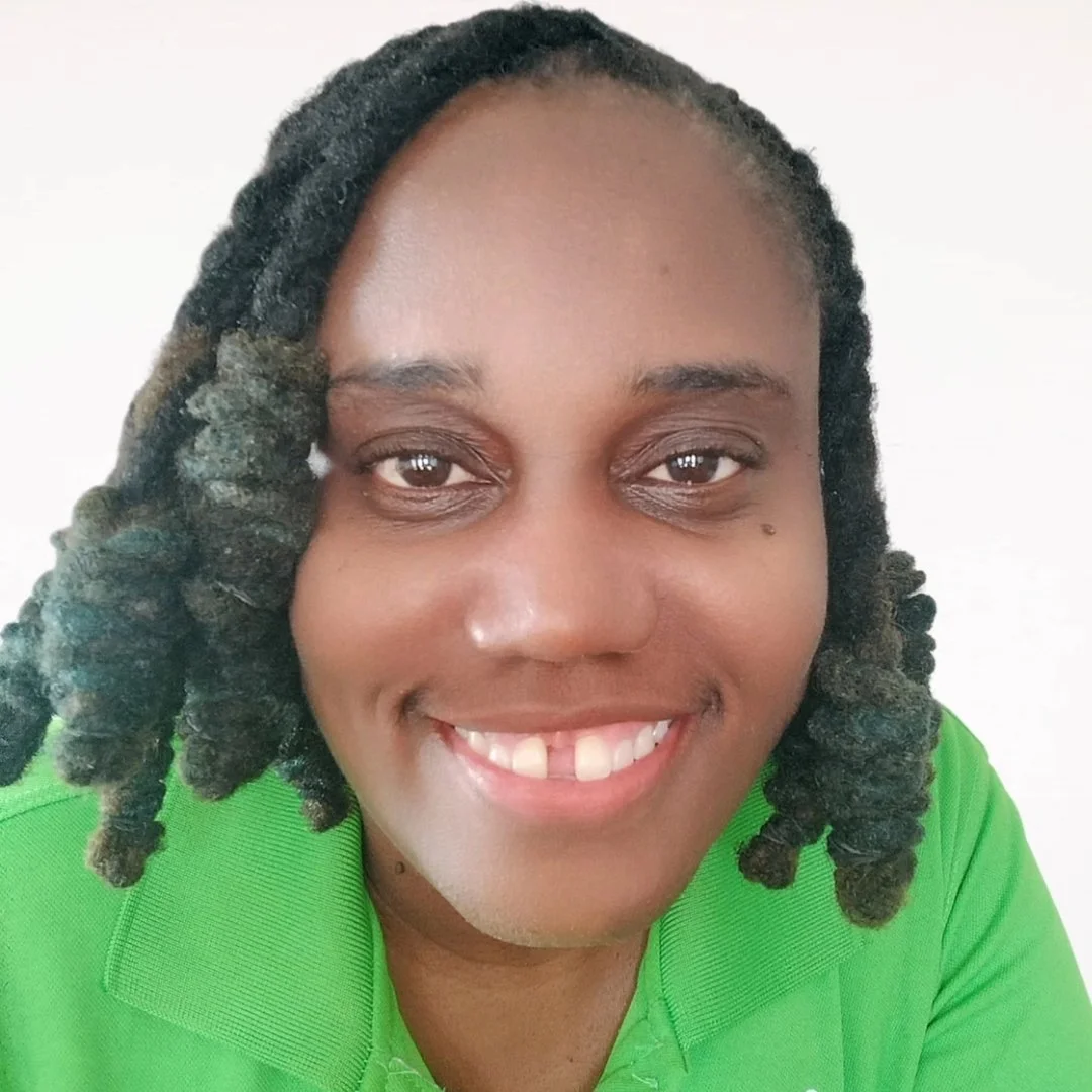 A woman with dark skin and shoulder-length twisted hair, smiling, wearing a green collared shirt.