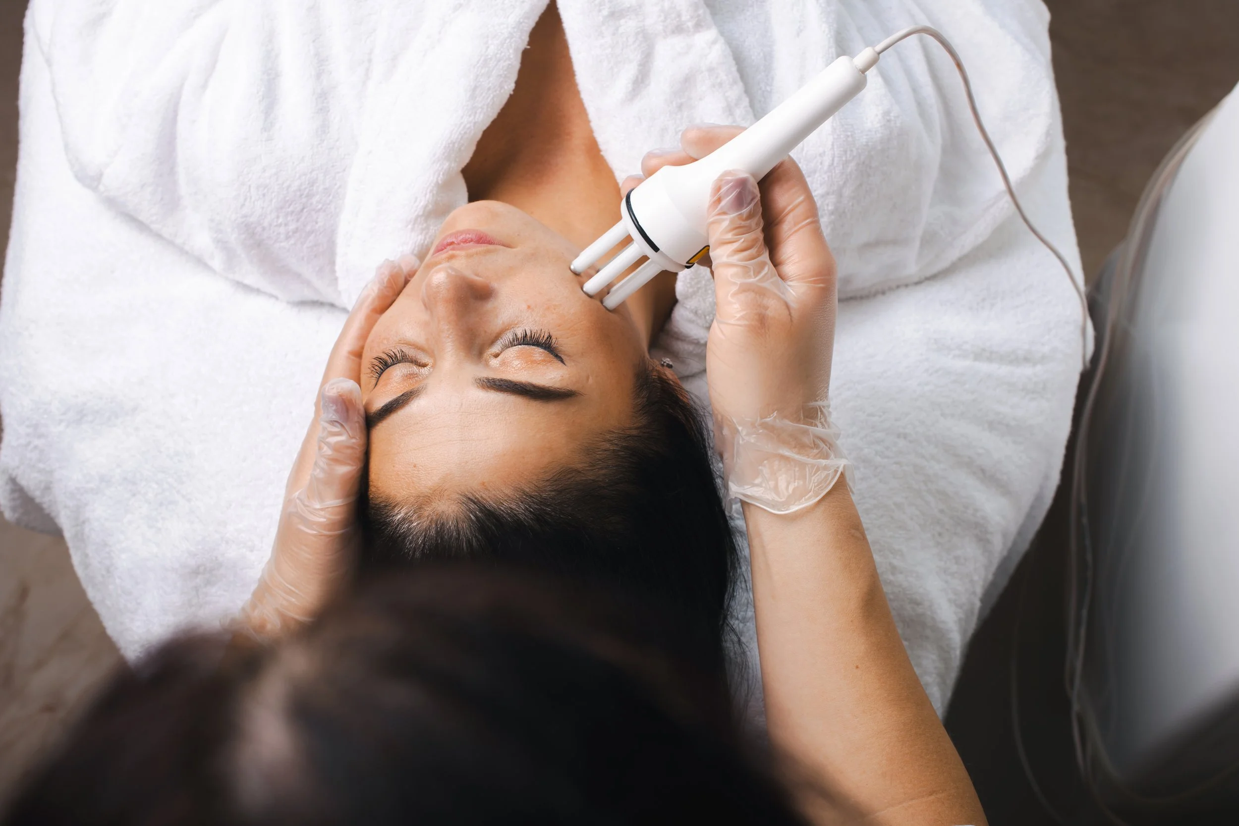 A woman receiving a facial treatment with a handheld device at a spa or clinic.