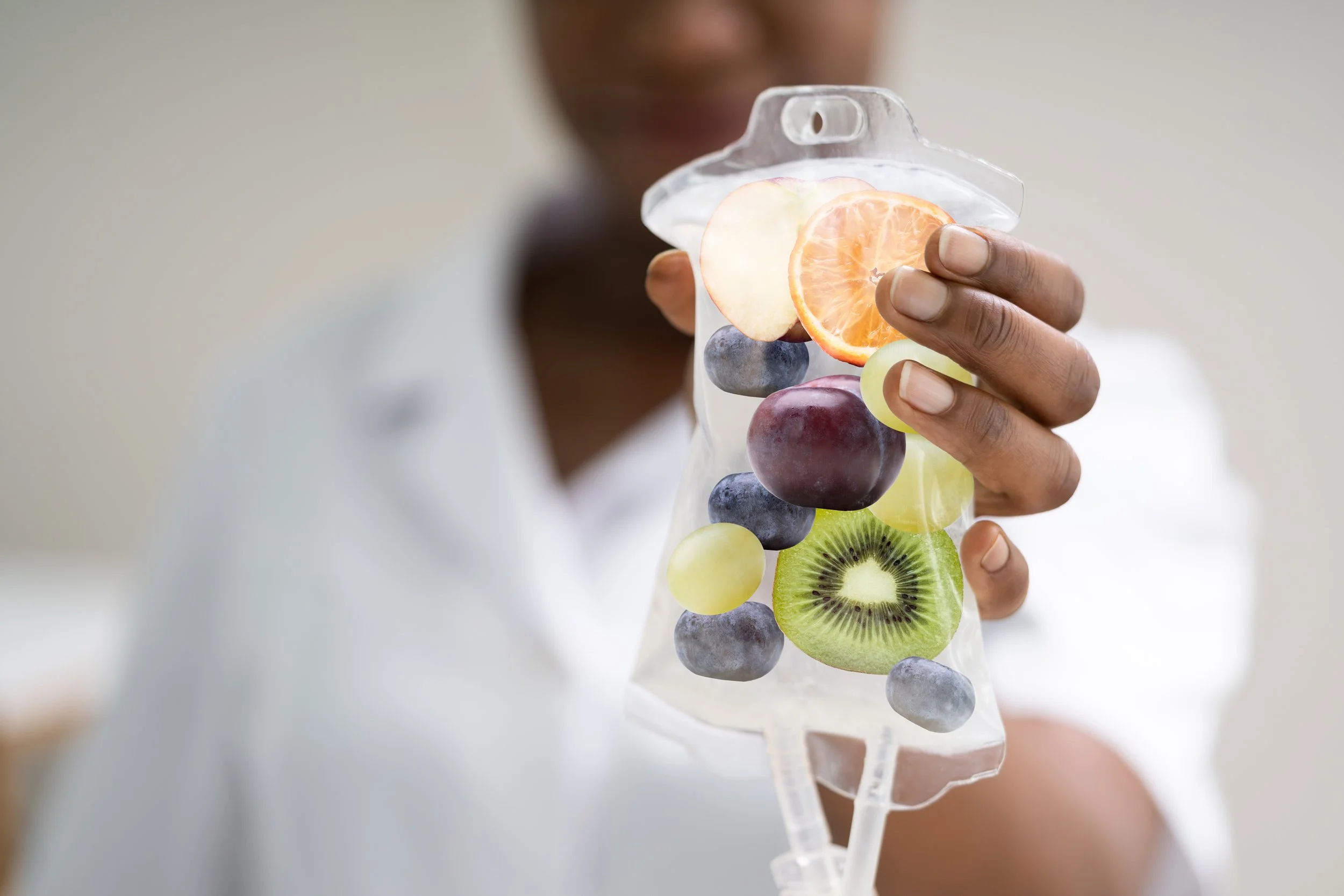 Person holding a transparent medical eye drop container filled with various sliced fruits including apple, orange, grape, kiwi, and blueberry.