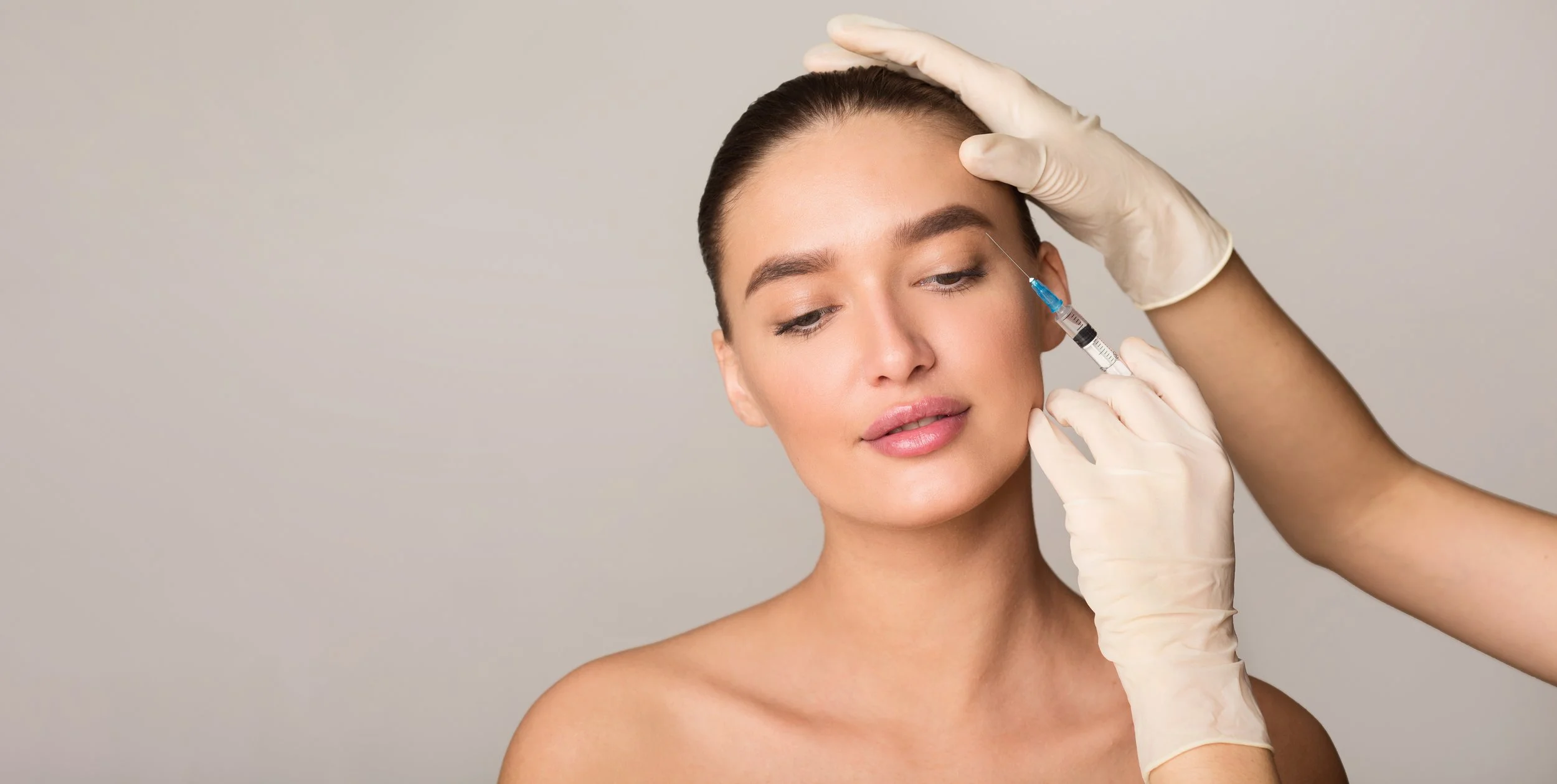 A woman receiving a cosmetic injection in her face from a healthcare professional wearing gloves.