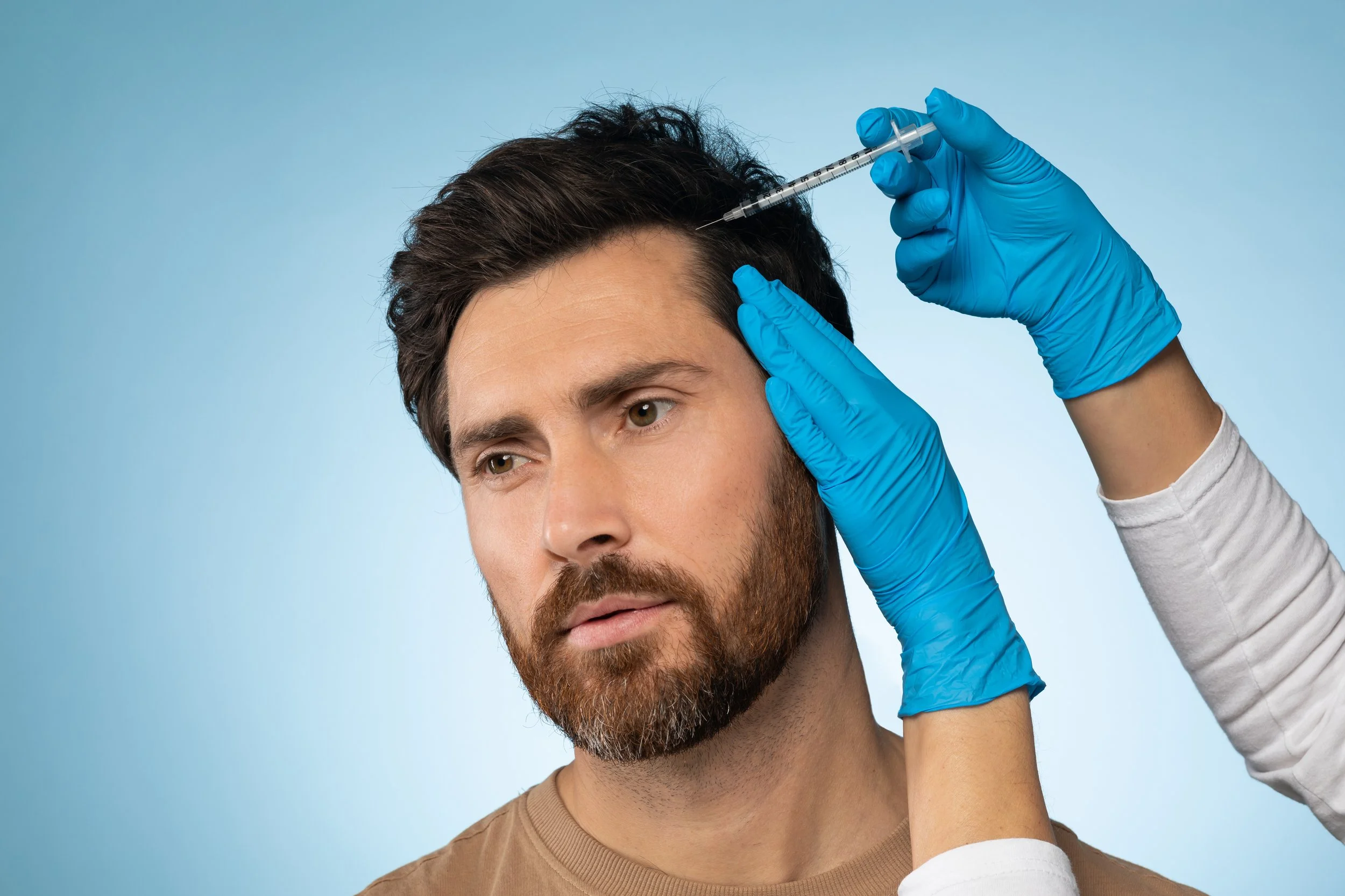 A man receives a forehead injection from a healthcare professional wearing blue gloves against a blue background.
