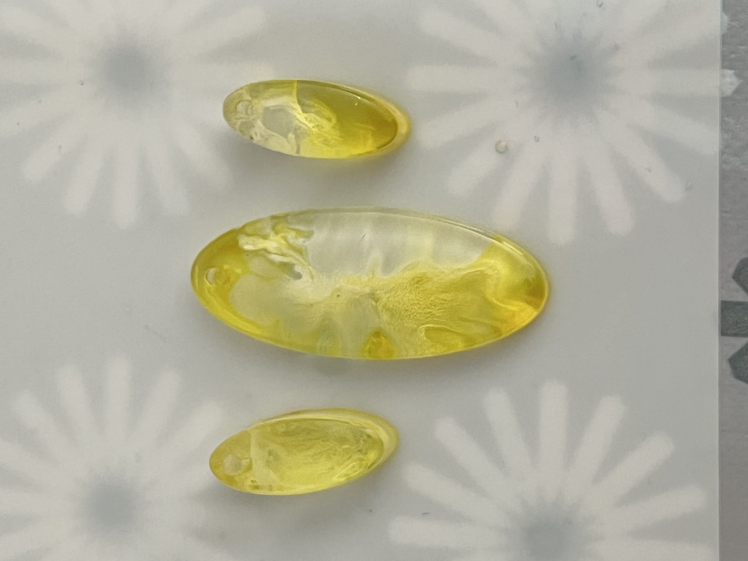 Three yellow capsules with clear gel interiors on a white surface with gray flower-like pattern.