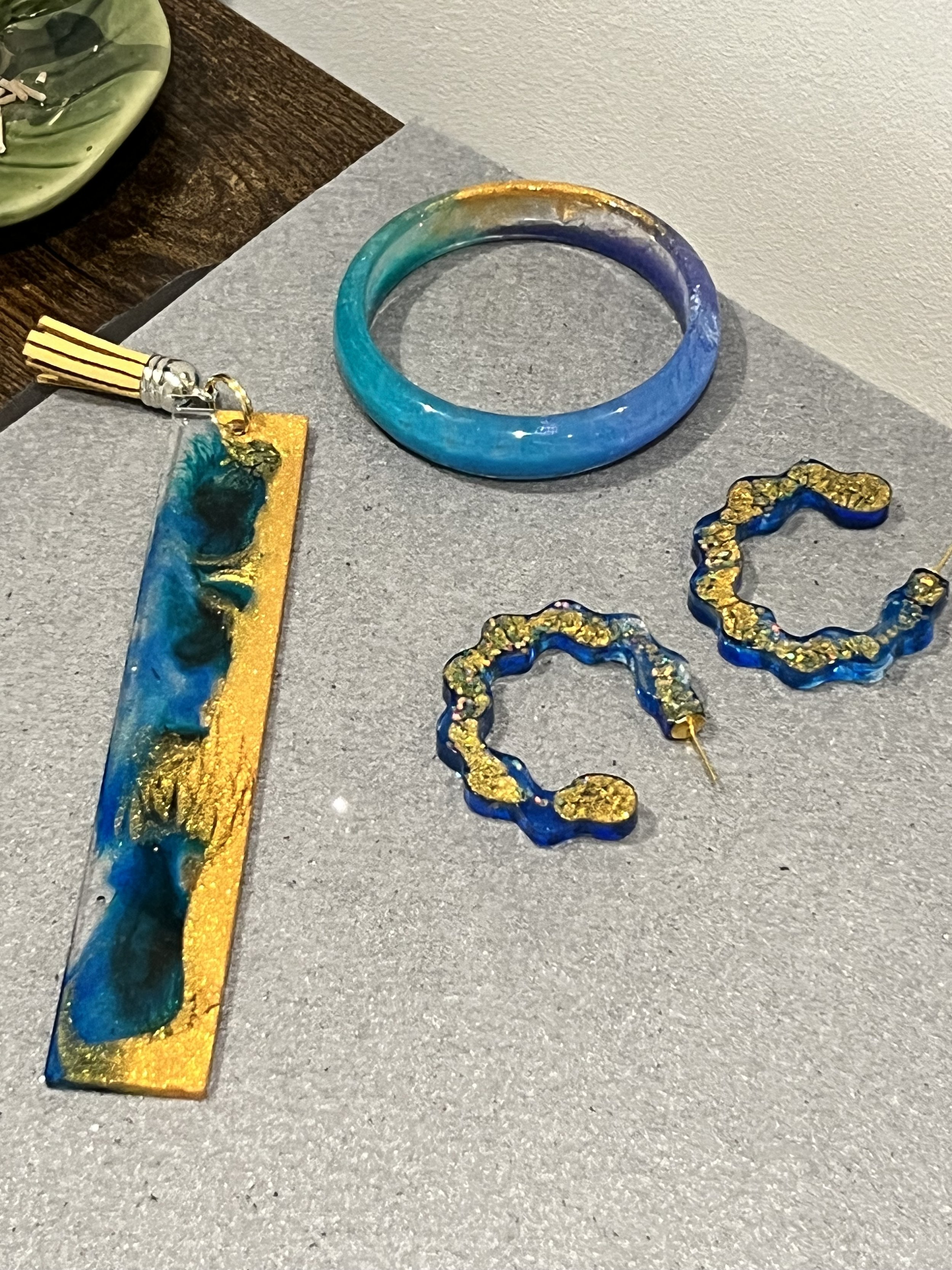 Blue and gold jewelry, including a bracelet, earrings, and a pendant, displayed on a gray surface.