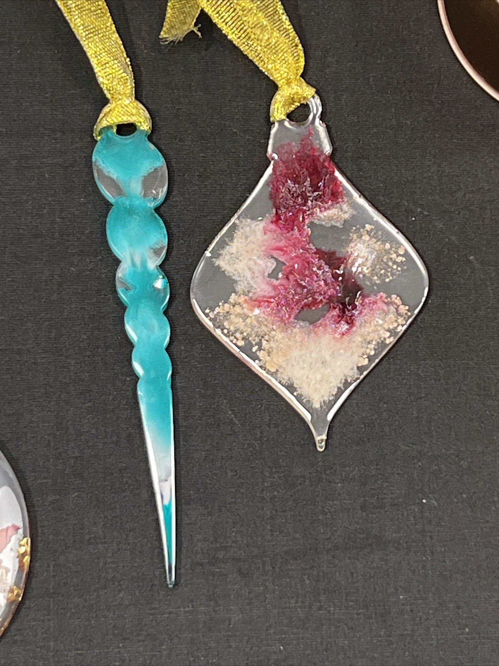 Decorative glass pendant necklaces, one with a blue and clear twisted design and the other with a pink, white, and red abstract pattern, displayed on a dark surface.