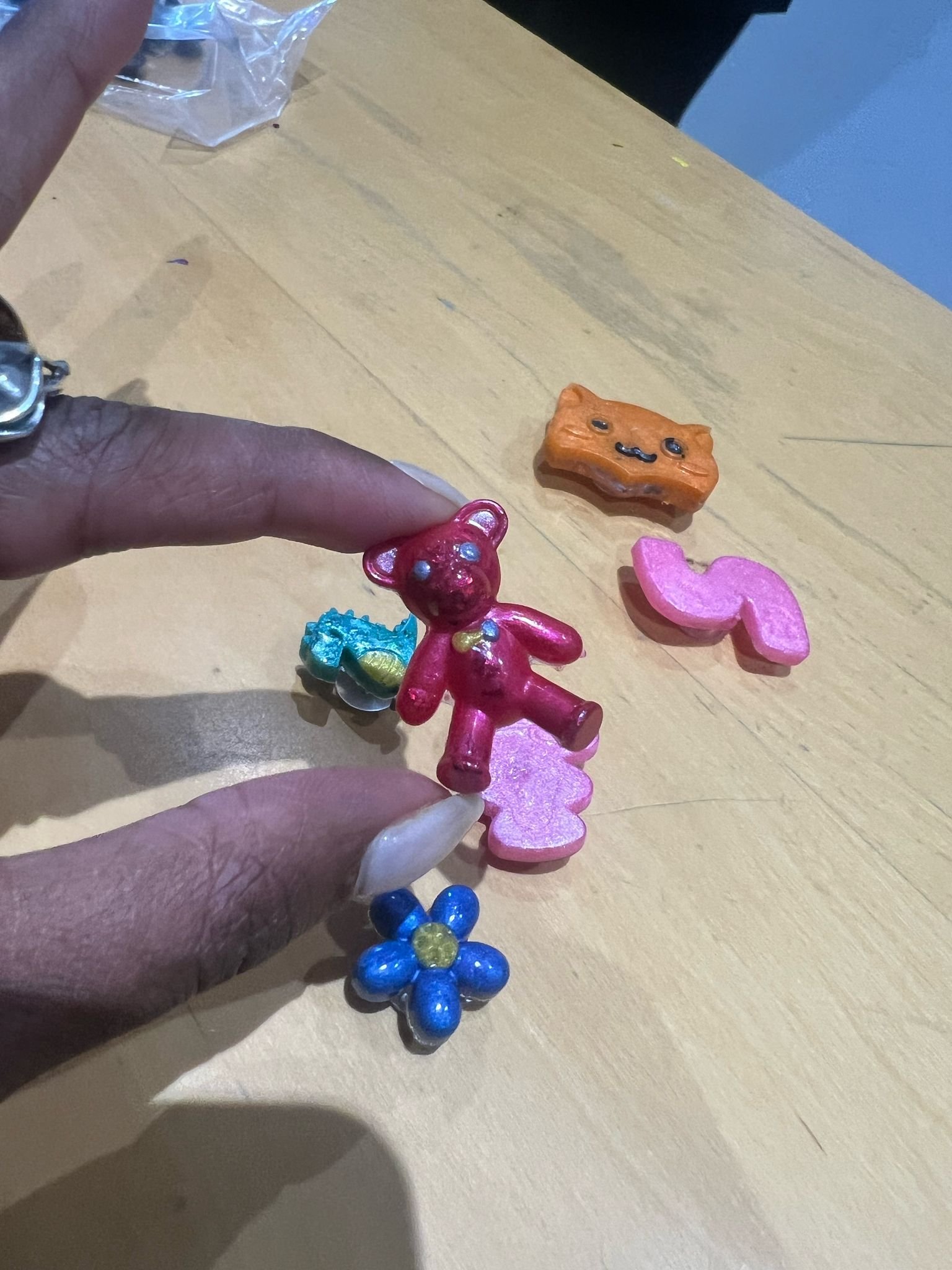Colorful toy figurines including a red teddy bear, a pink heart, an orange cat, a blue flower, and a small blue and yellow butterfly, arranged on a light wooden surface.