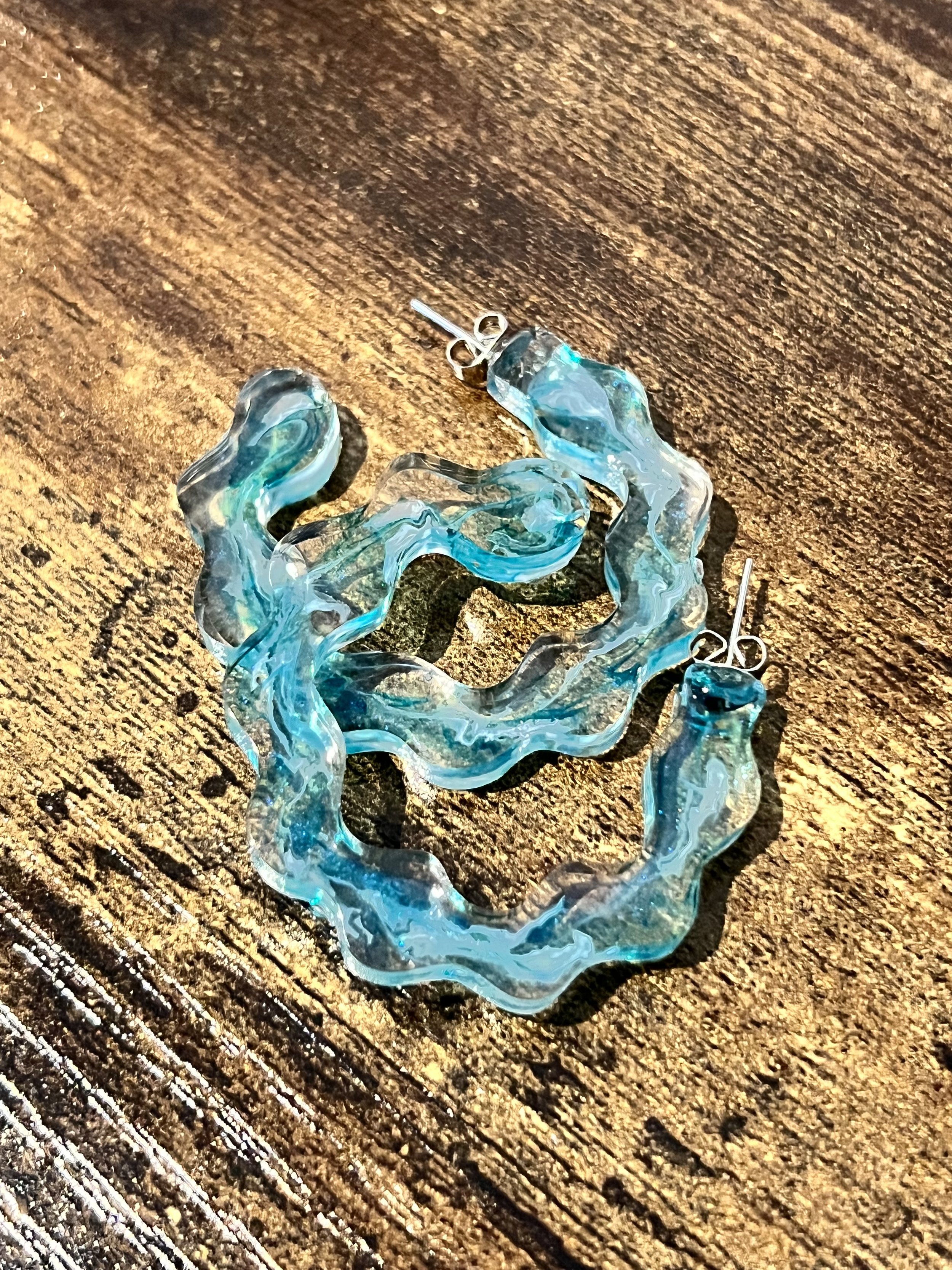 Blue and clear marbled resin earrings on a wooden surface.