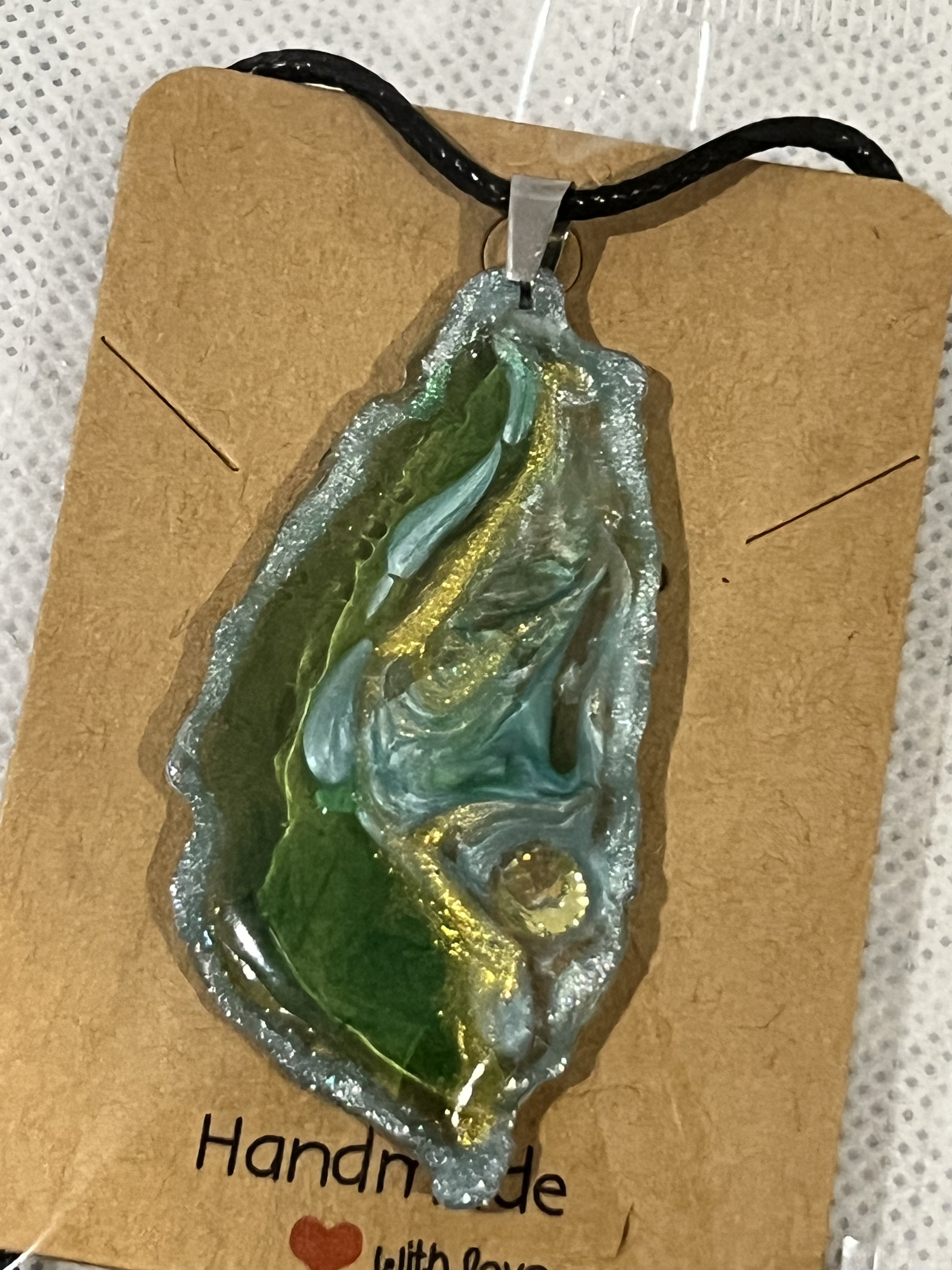 Handmade glass pendant with green, blue, and gold swirls on a leather cord.