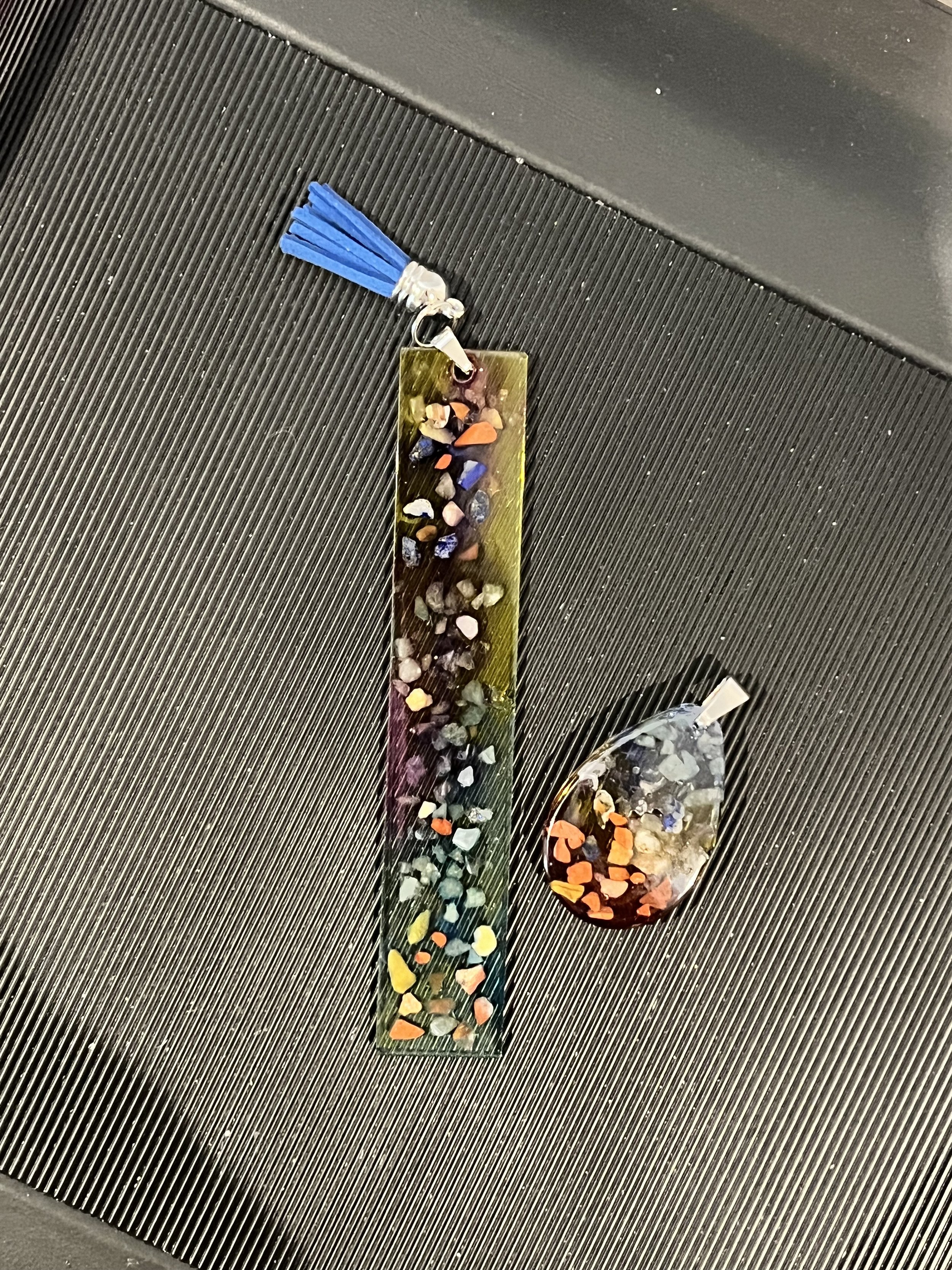 A colorful resin bookmark with small embedded stones and a blue tassel and a matching resin paperweight with embedded stones