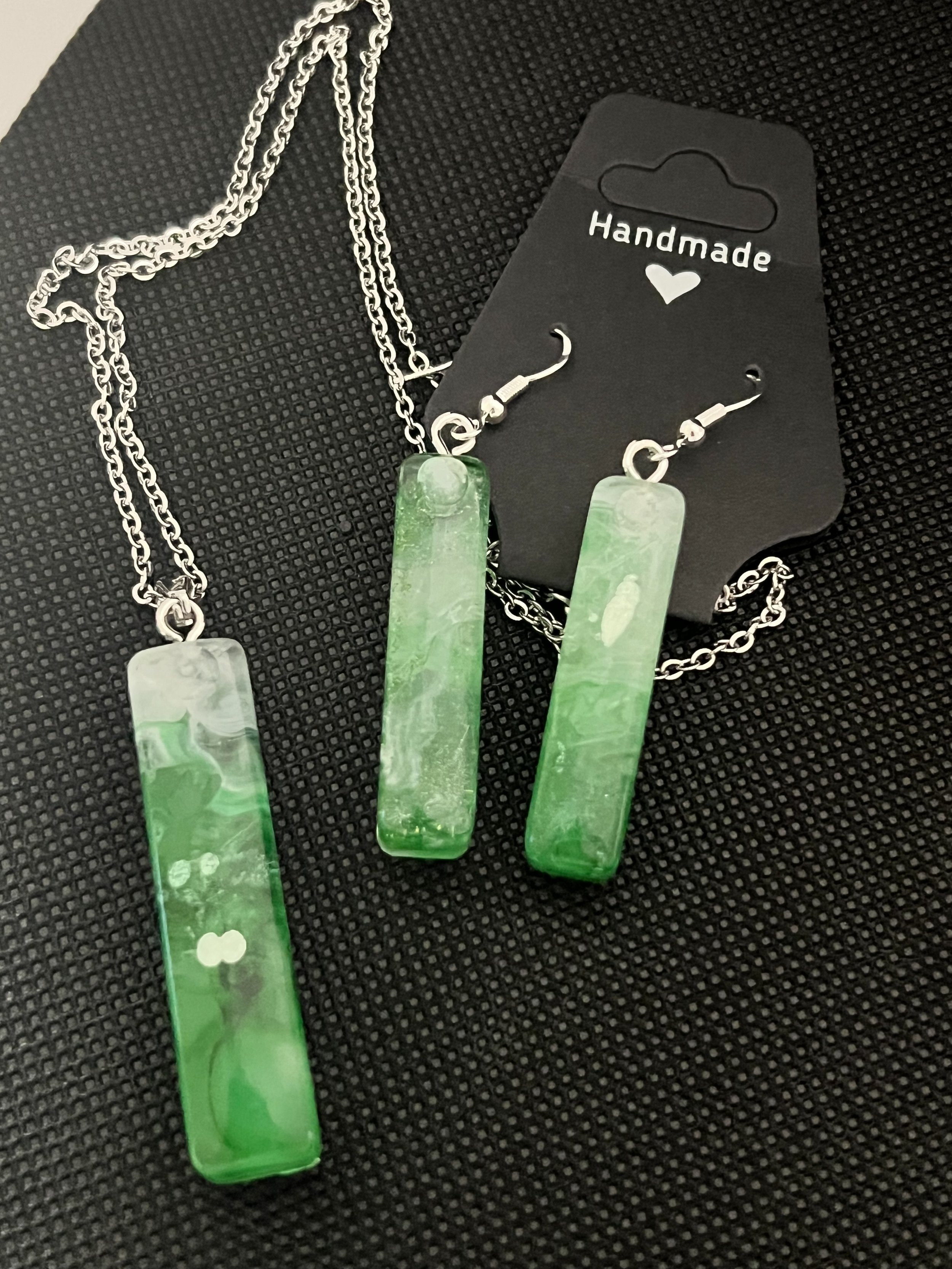 Green marbled rectangle pendant necklace and matching earrings on black background, labeled Handmade with a heart on black display card.