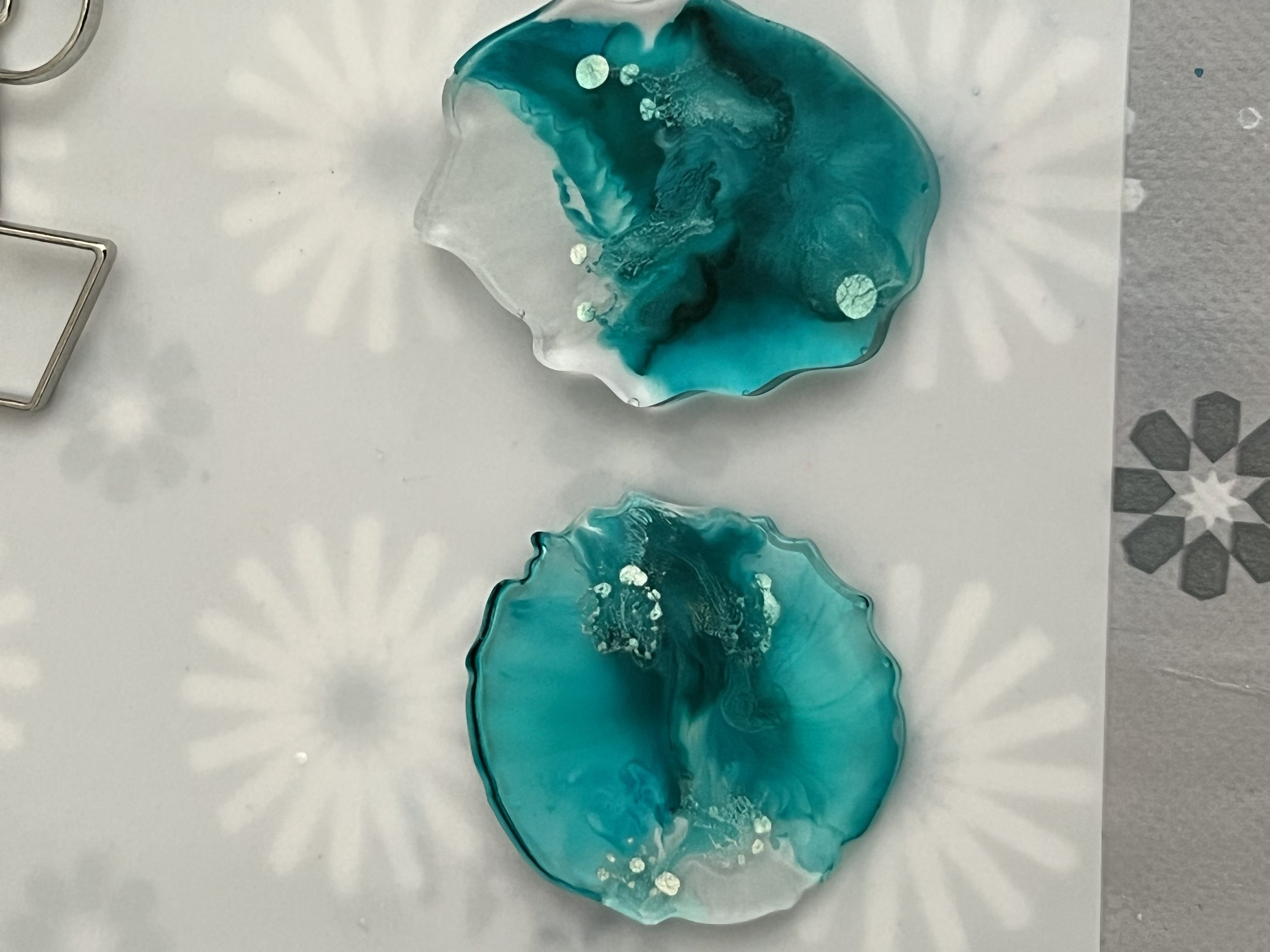 Two irregularly shaped glass pieces with swirling blue and turquoise colors on a white surface with starburst shadows.