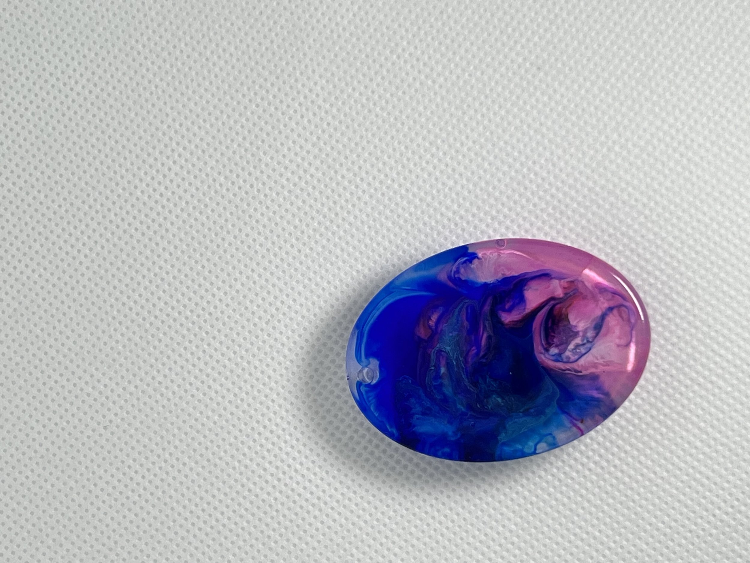 A colorful, abstract marble with swirls of blue, pink, and purple on a white textured surface.