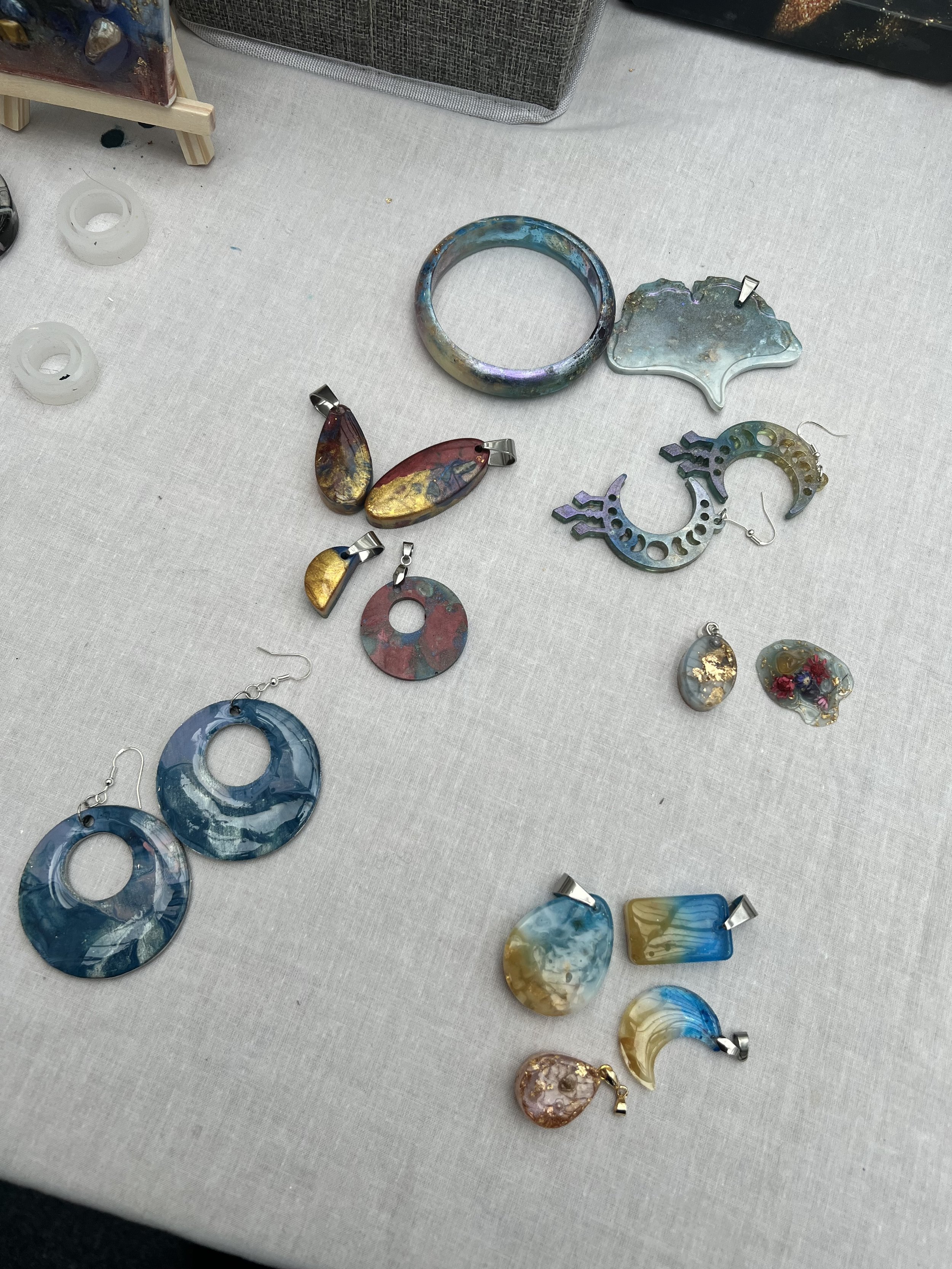 Assorted colorful glass and metal earrings and jewelry pieces on a white fabric surface.