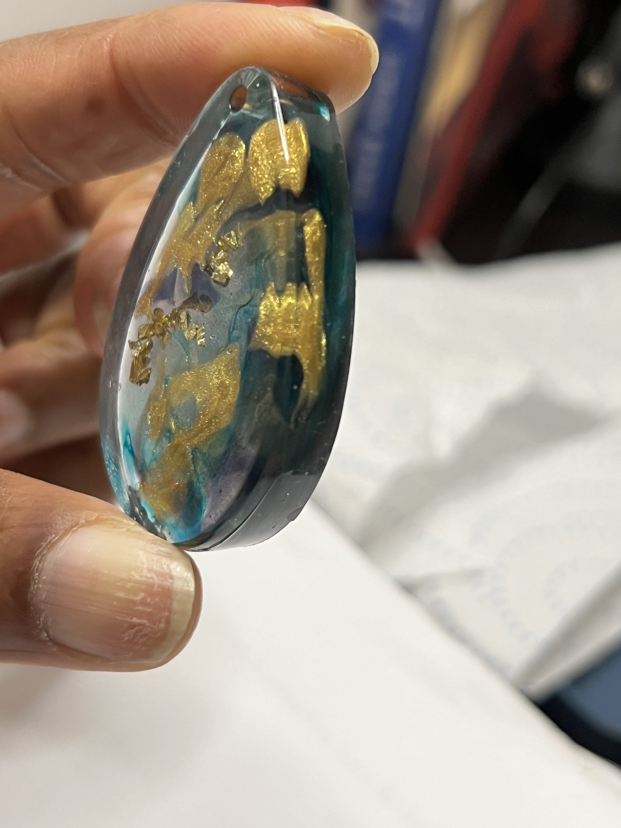 Close-up of an oval-shaped glass paperweight with swirling blue, black, and gold interior designs, held between fingers.