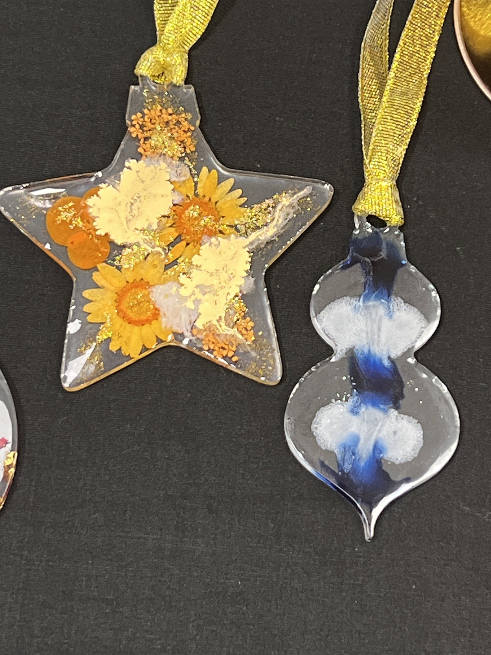 Decorative glass medals decorated with flowers and abstract paint designs, hanging from yellow ribbons.
