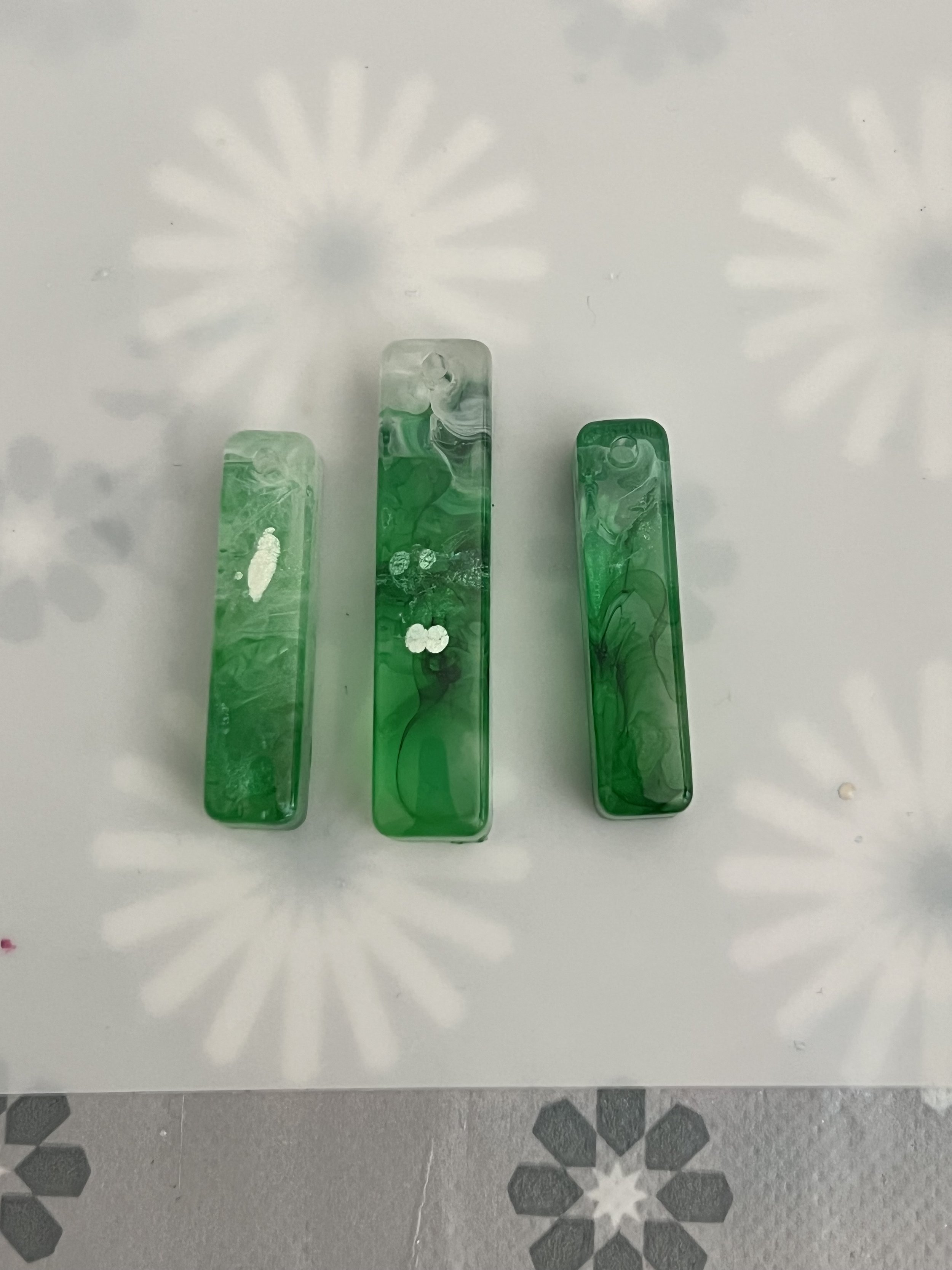 Three rectangular green marbled glass soap dishes on a white surface with floral patterns cast shadows.