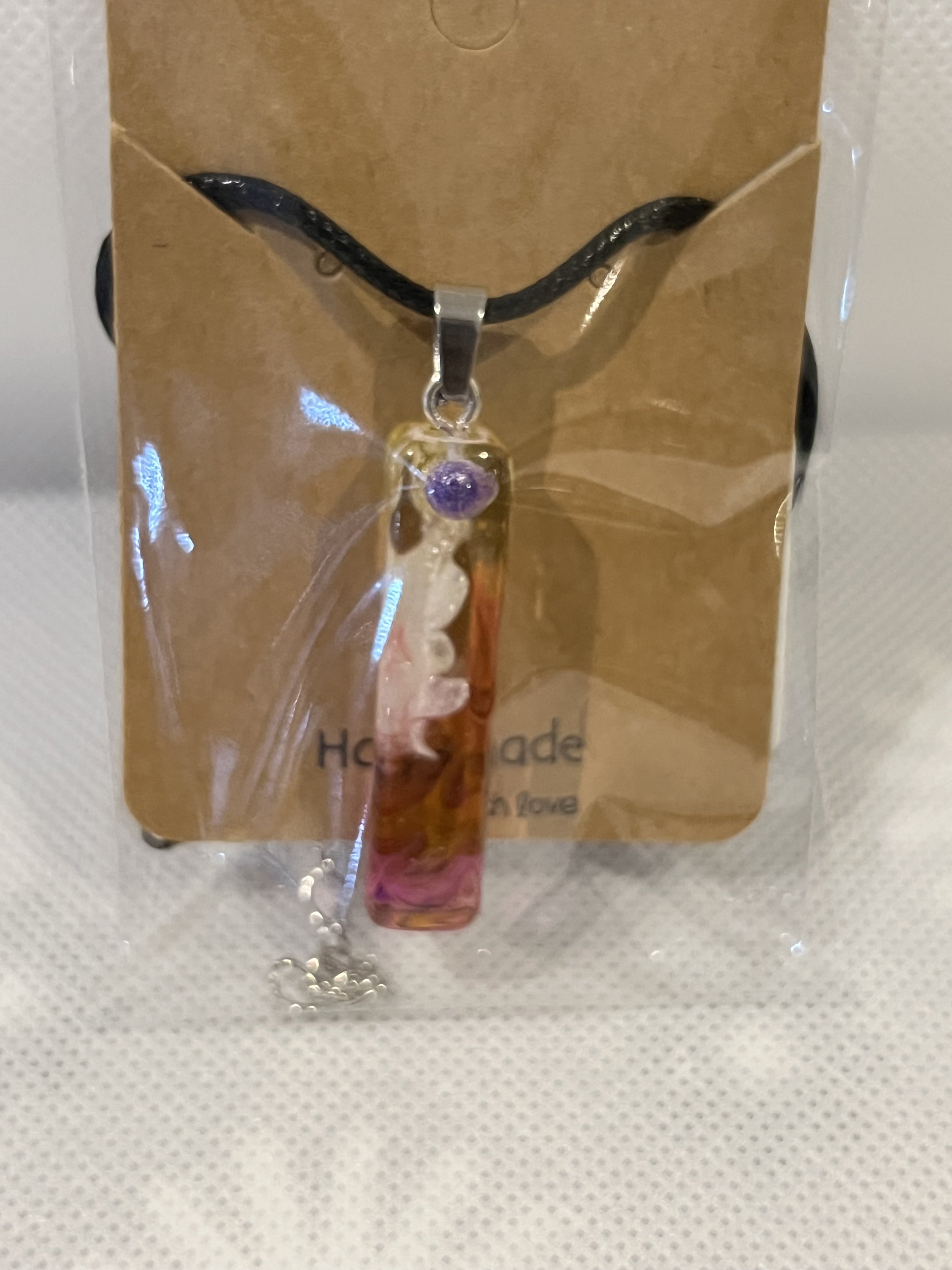 Colorful glass pendant necklace with a purple accent on a black cord, packaged on a cardboard backing.