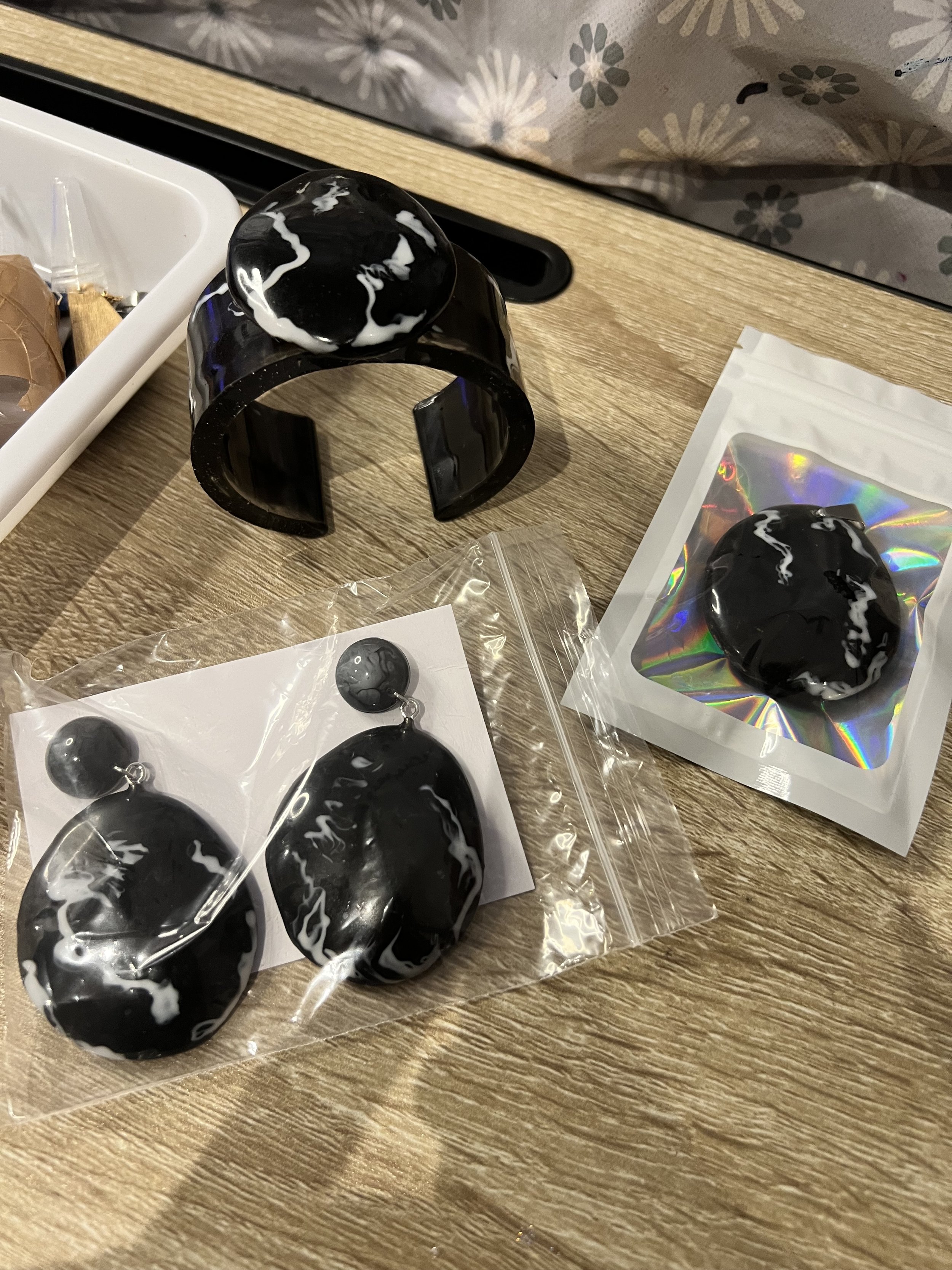 Black and white marbled jewelry, including a pair of earrings with circular and oval shapes and a large bracelet, displayed on a wooden surface.